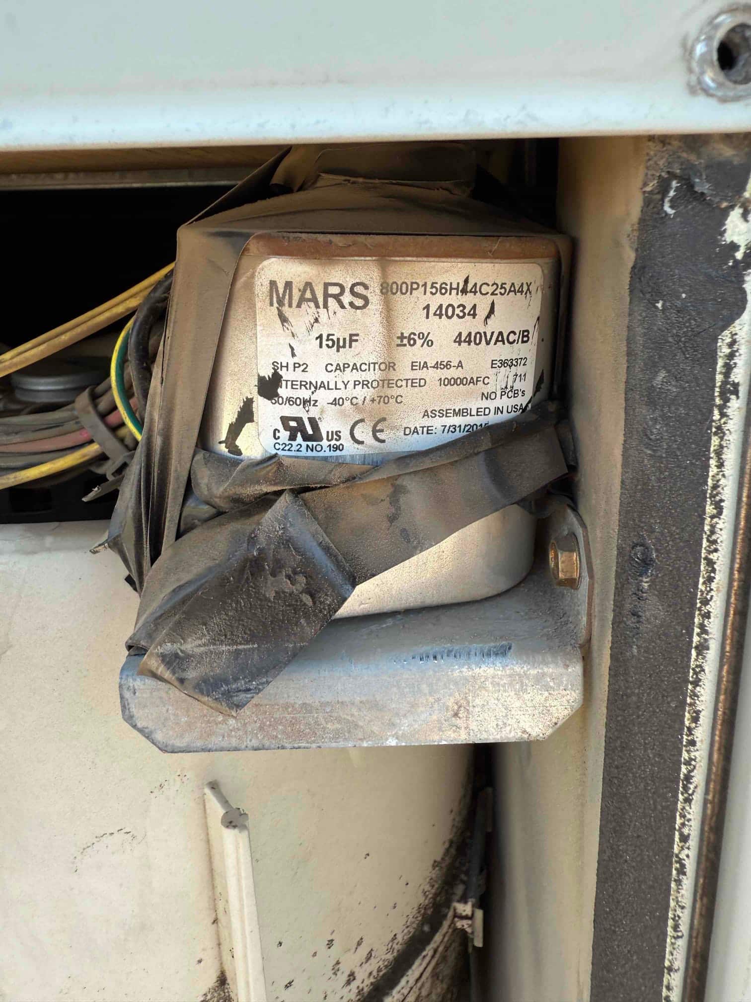 Dual-run capacitor inside the condenser compartment with taped insulation, labeled 15 μF ±6% and 440VAC/B rating.