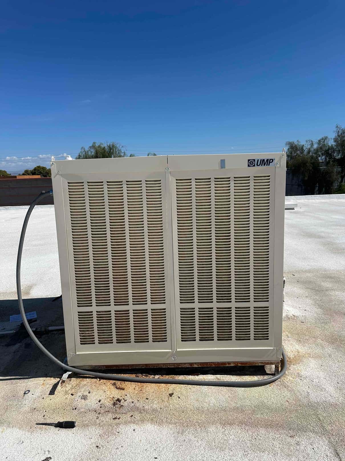 Evaporative cooler housing installed on rooftop with secured conduit and leveled base, photographed during clear daylight conditions.