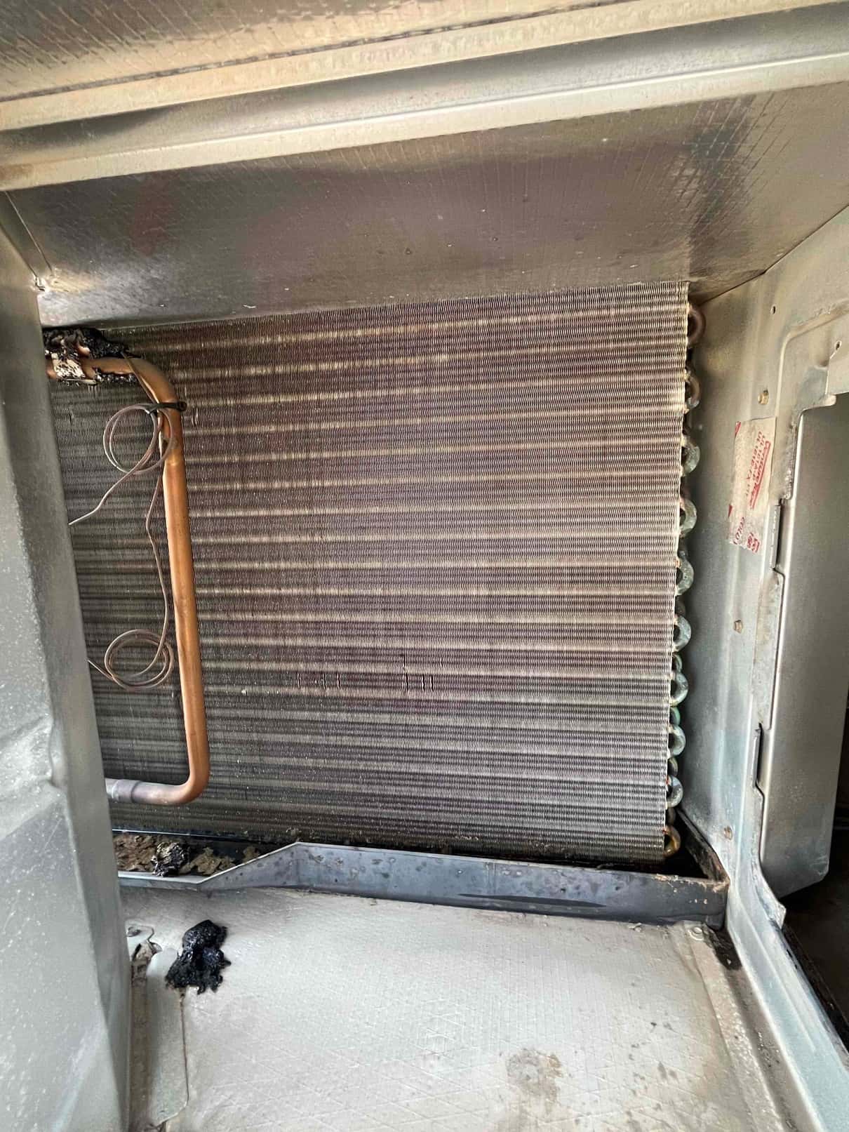 Evaporator coil inside an air handler, showing clean fins, copper tubing, and drain pan area with some debris.