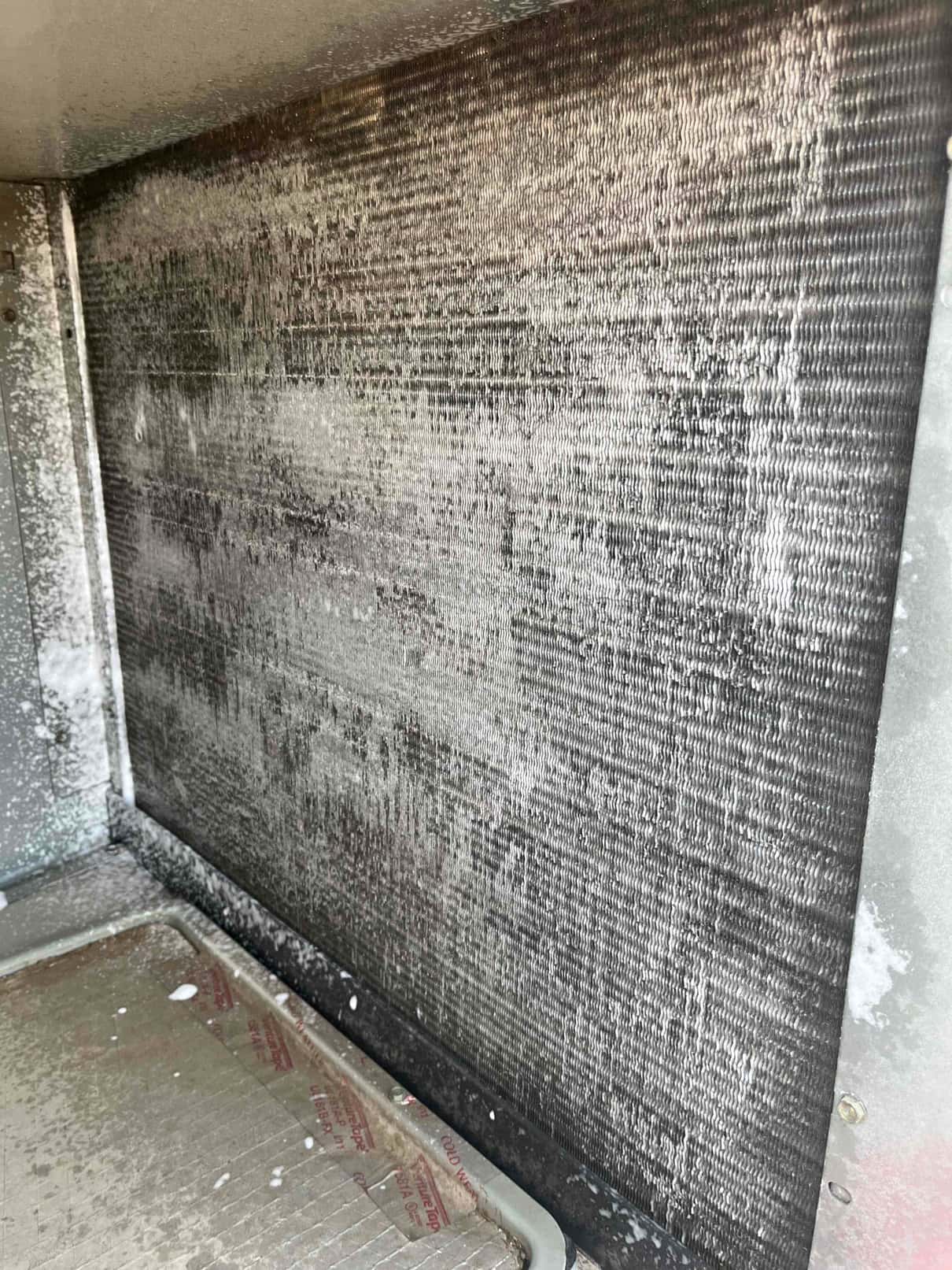 Evaporator coil surface inside an air handler showing heavy dust and debris accumulation across the fins and drain pan area.
