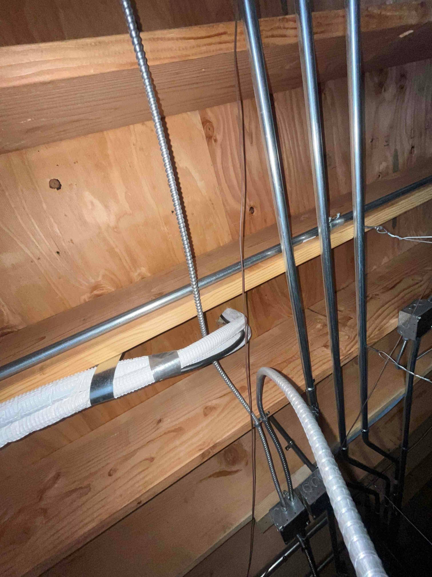 Flexible conduit and electrical cables secured along attic framing near HVAC equipment, showing routing and support with metal straps.