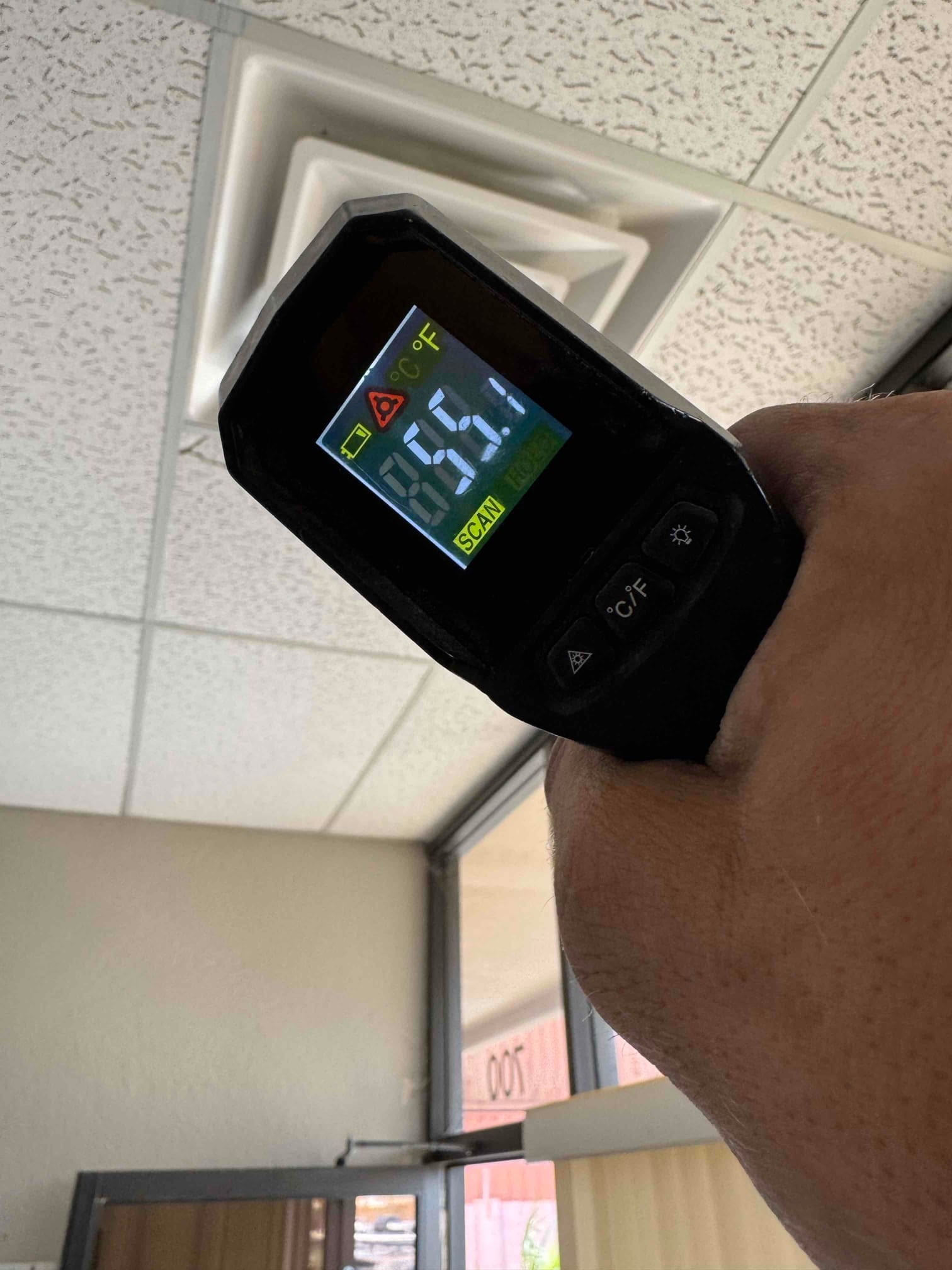 Infrared thermometer aimed at a ceiling supply register shows 55.1 degrees Fahrenheit during cooling operation.