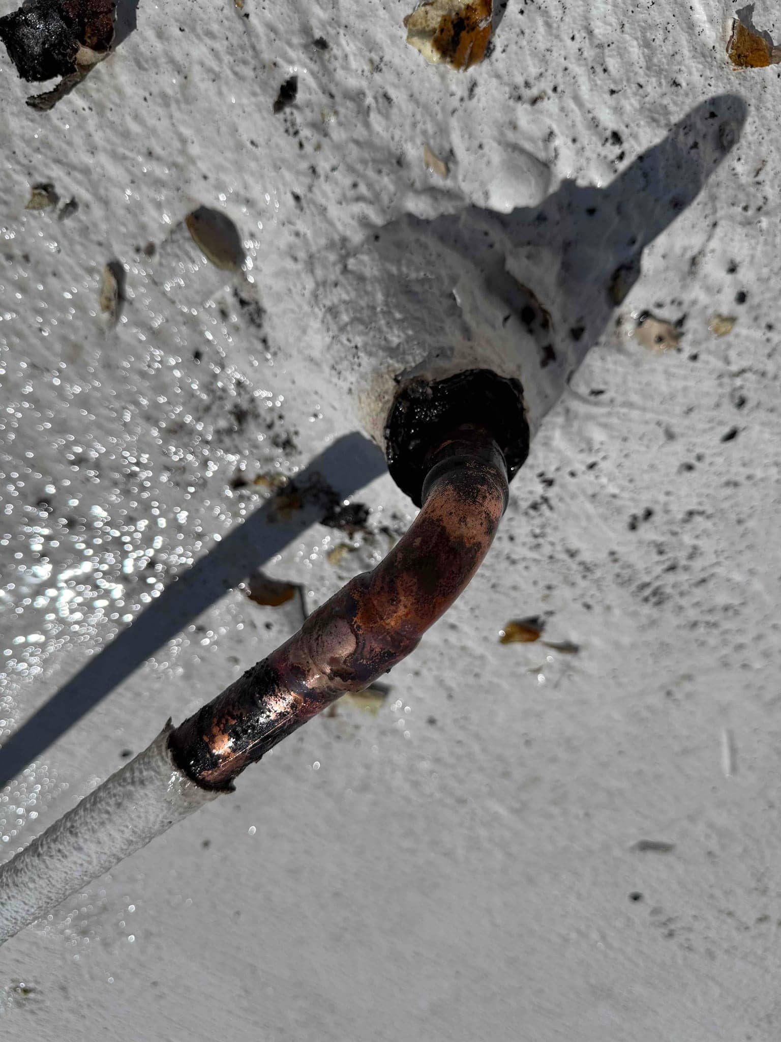 Insulated copper refrigerant line penetrating a sealed roof curb, showing a cleaned and brazed joint at the entry.