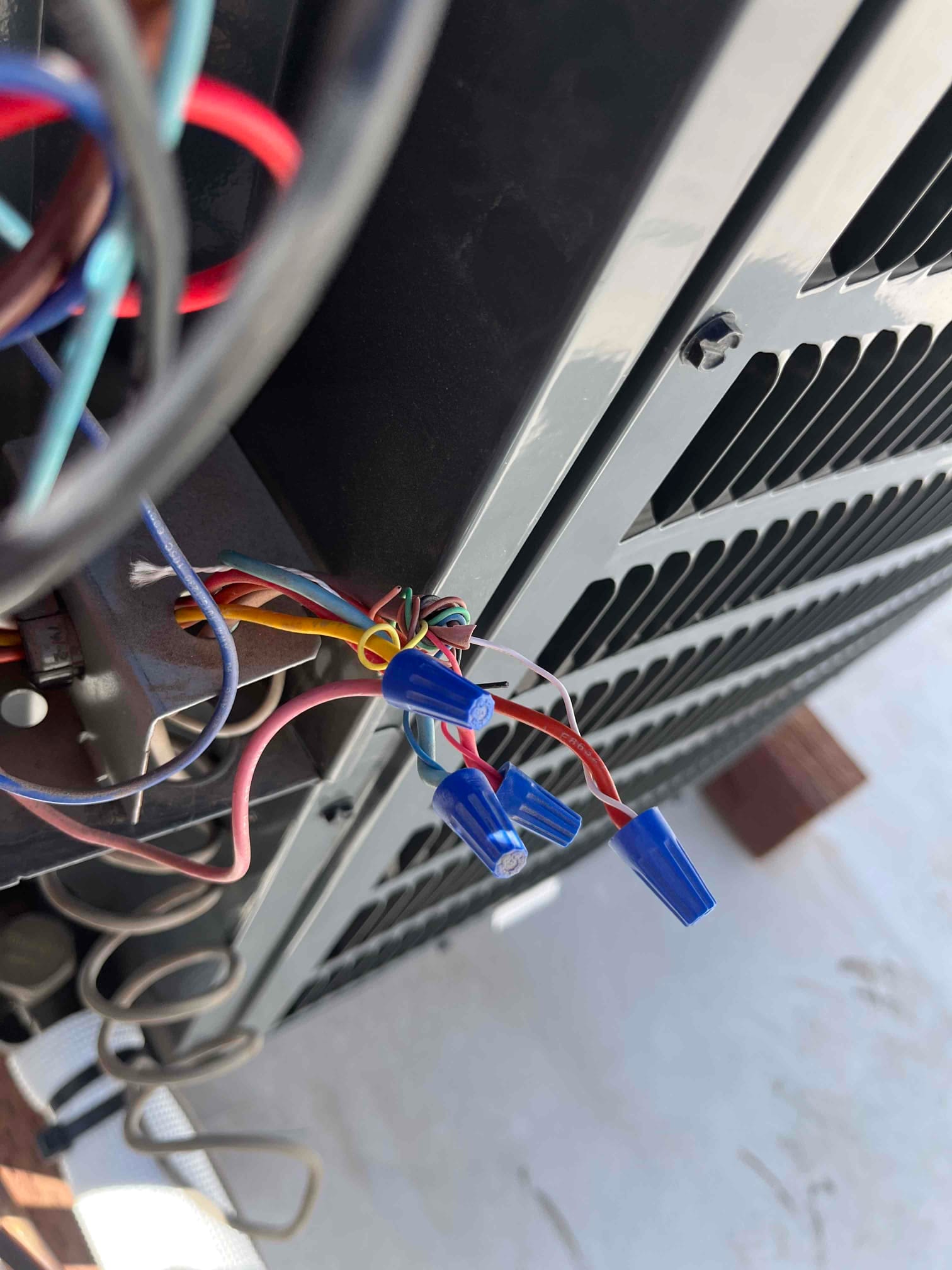 Low-voltage thermostat wiring with blue wire nuts connected near the outdoor condenser cabinet, showing twisted conductors and insulated splices.