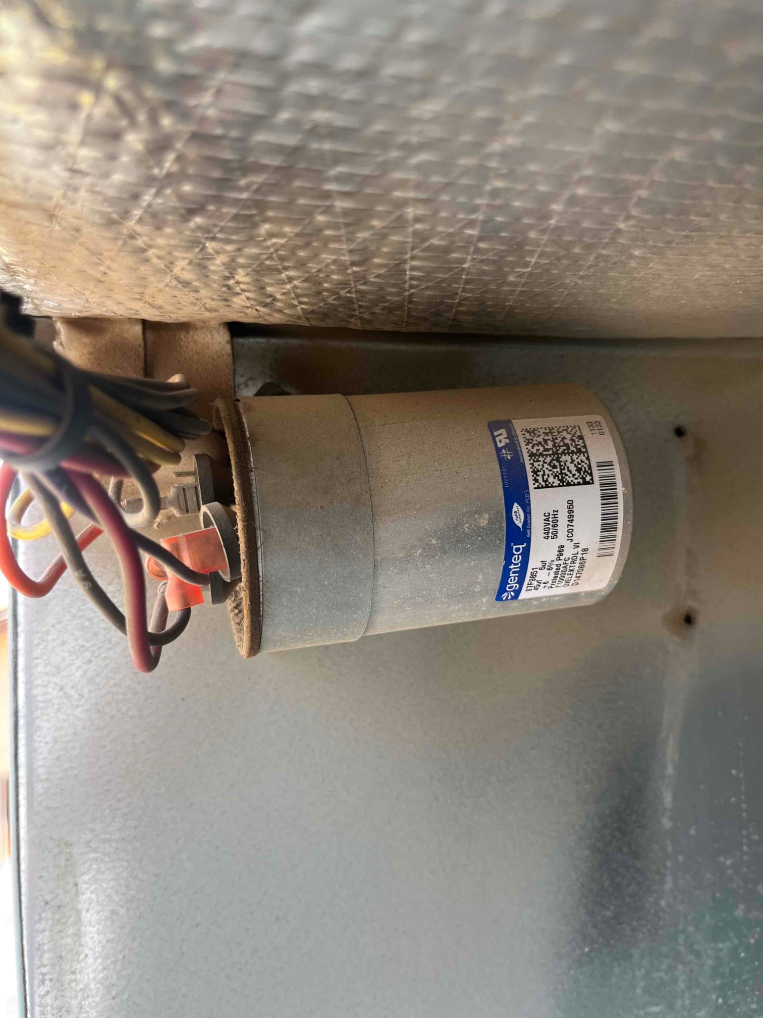 Metal can run capacitor mounted inside the condenser cabinet with connected wires and clean housing, showing a printed specification label.