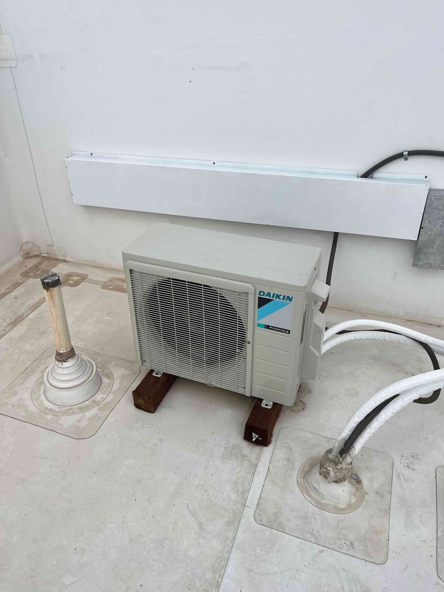 Mini-split outdoor condenser set on riser blocks with insulated line set and electrical conduit routed along the wall.