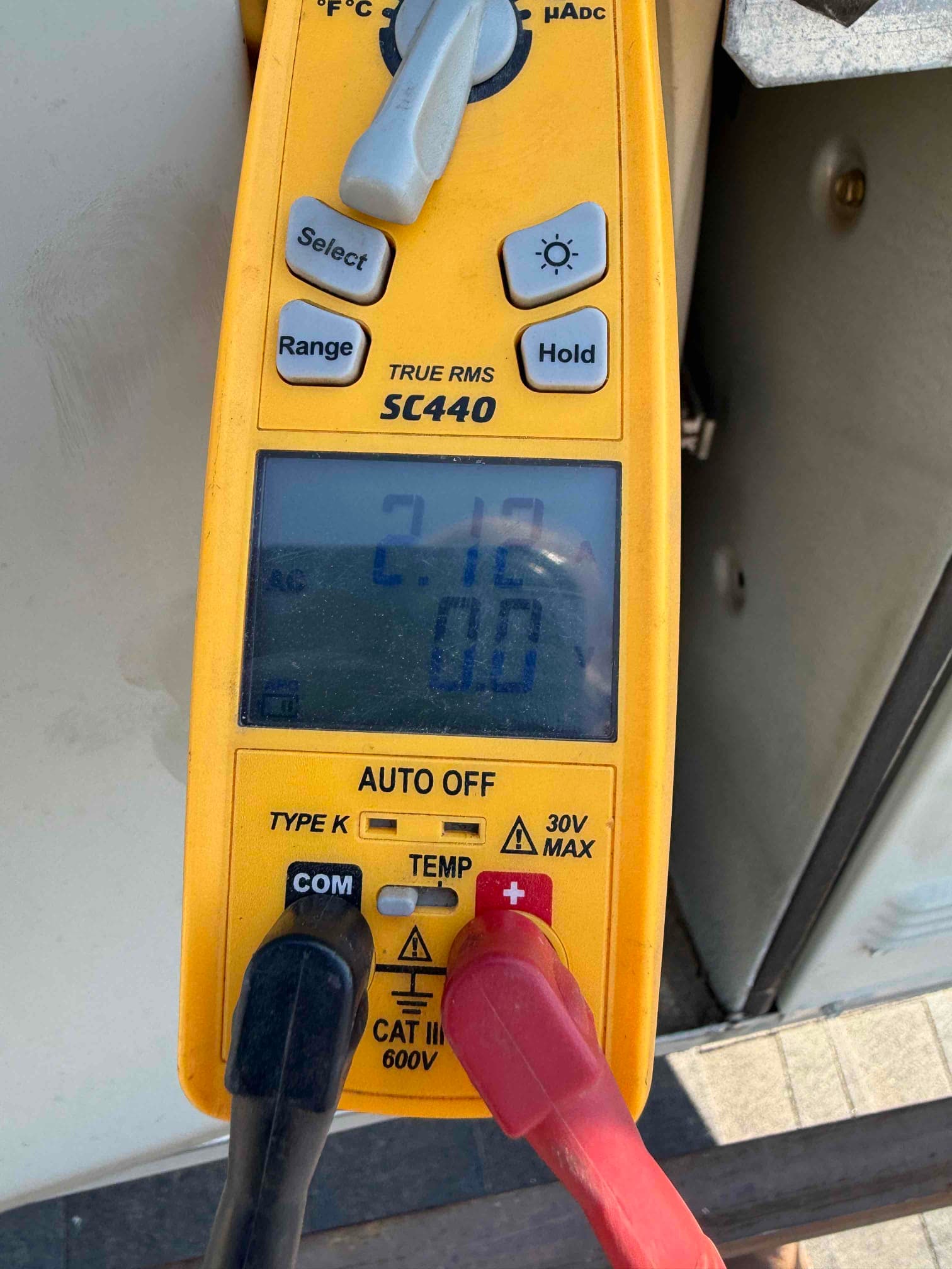 Multimeter display shows 2.12 A on the clamp measurement while connected near the outdoor unit.