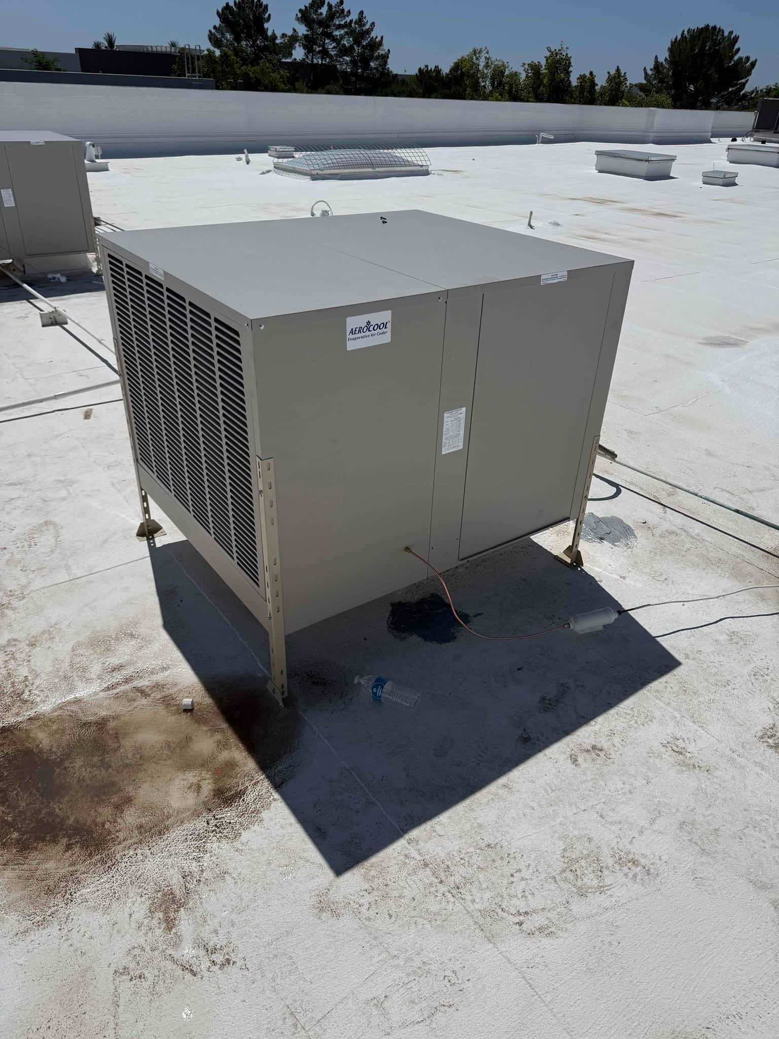 New rooftop evaporative cooler installed on a flat roof with secured mounting legs and surrounding rooftop equipment visible.