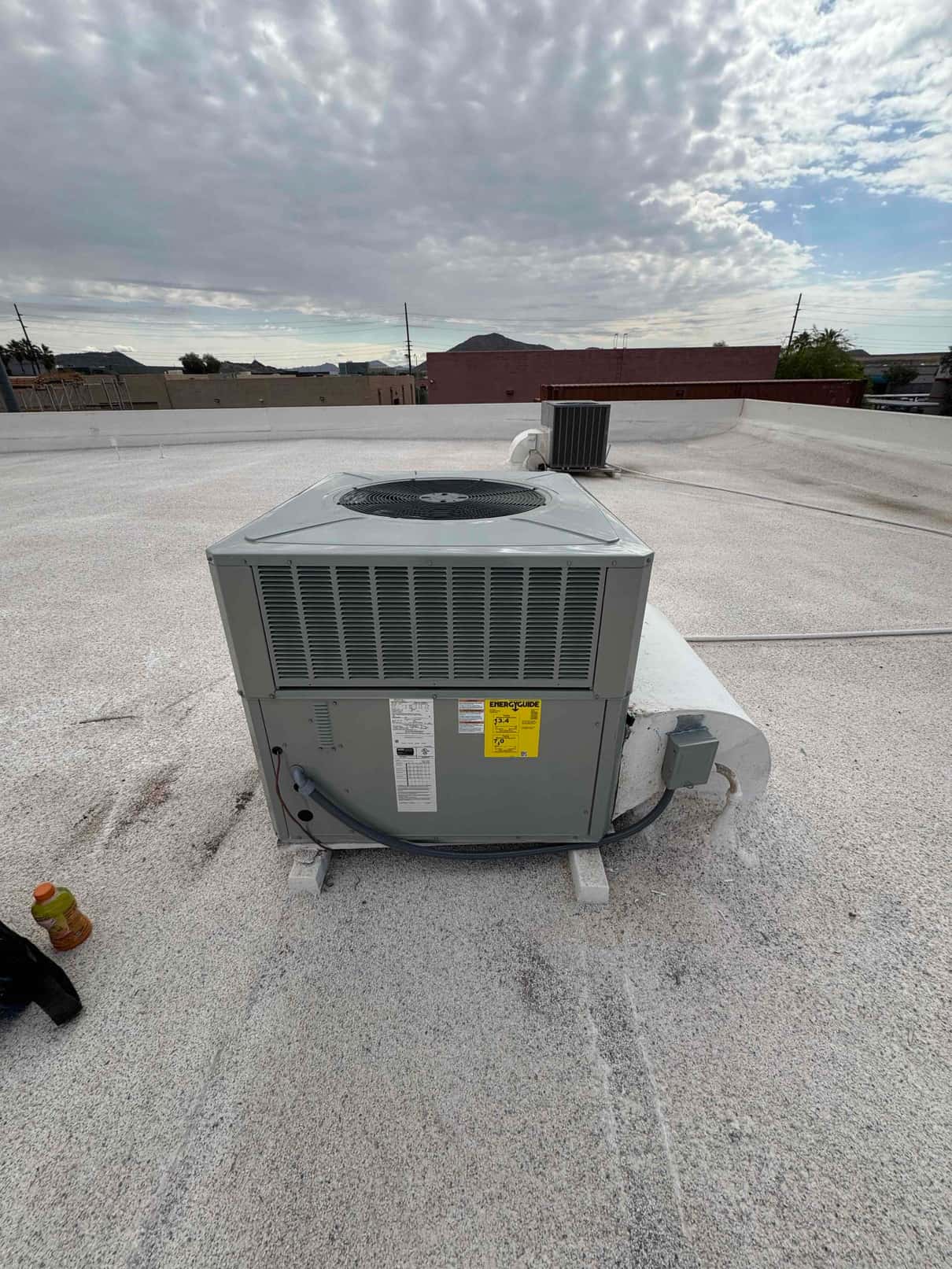 New rooftop heat pump condenser set on blocks with sealed line set and weatherproof disconnect conduit visible.