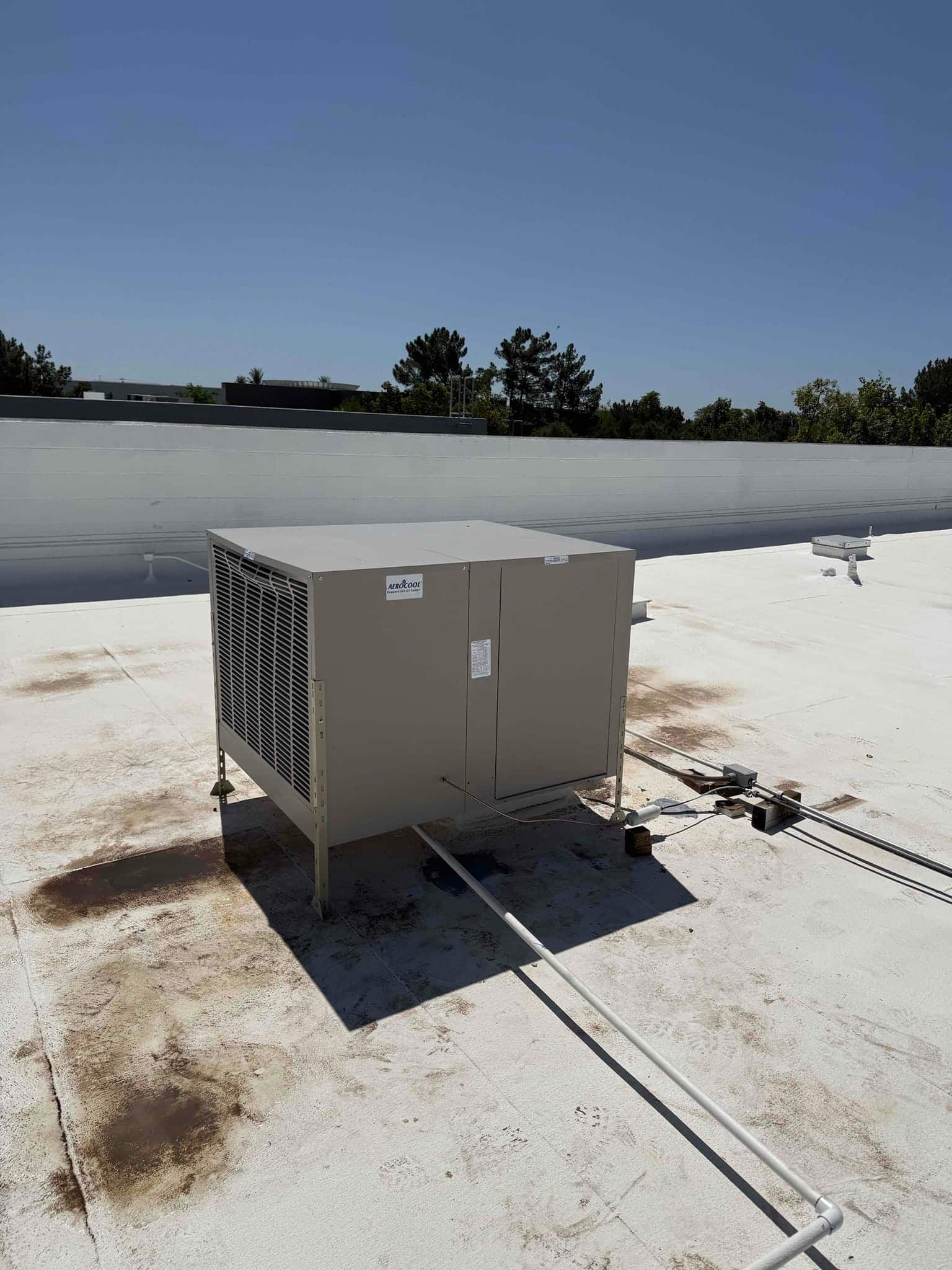 New rooftop HVAC unit set on supports with connected electrical conduits and condensate drain on a finished roof surface.