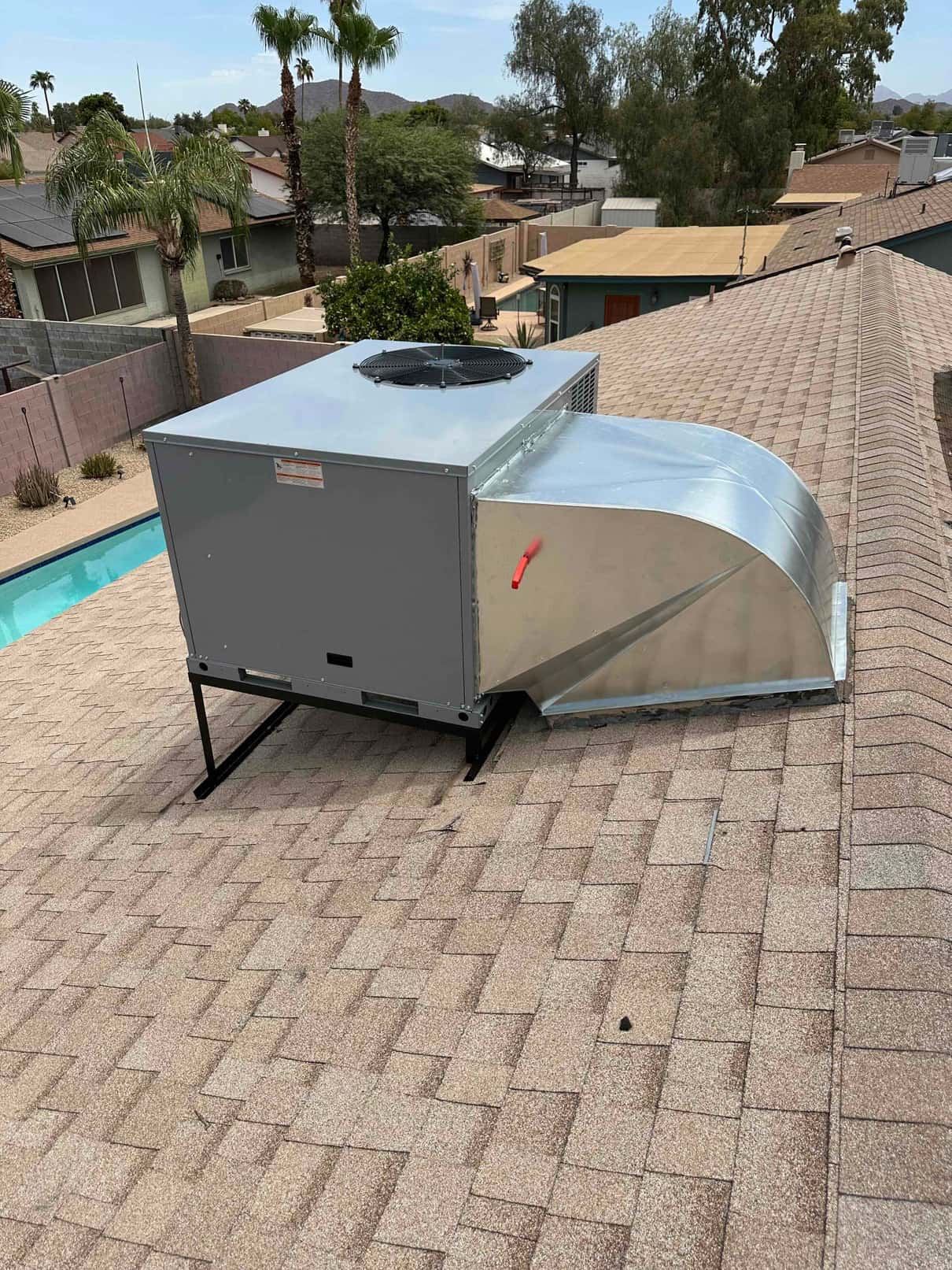 New rooftop package HVAC unit set on a metal stand with sheet metal curb adapter sealed to the shingle roof.