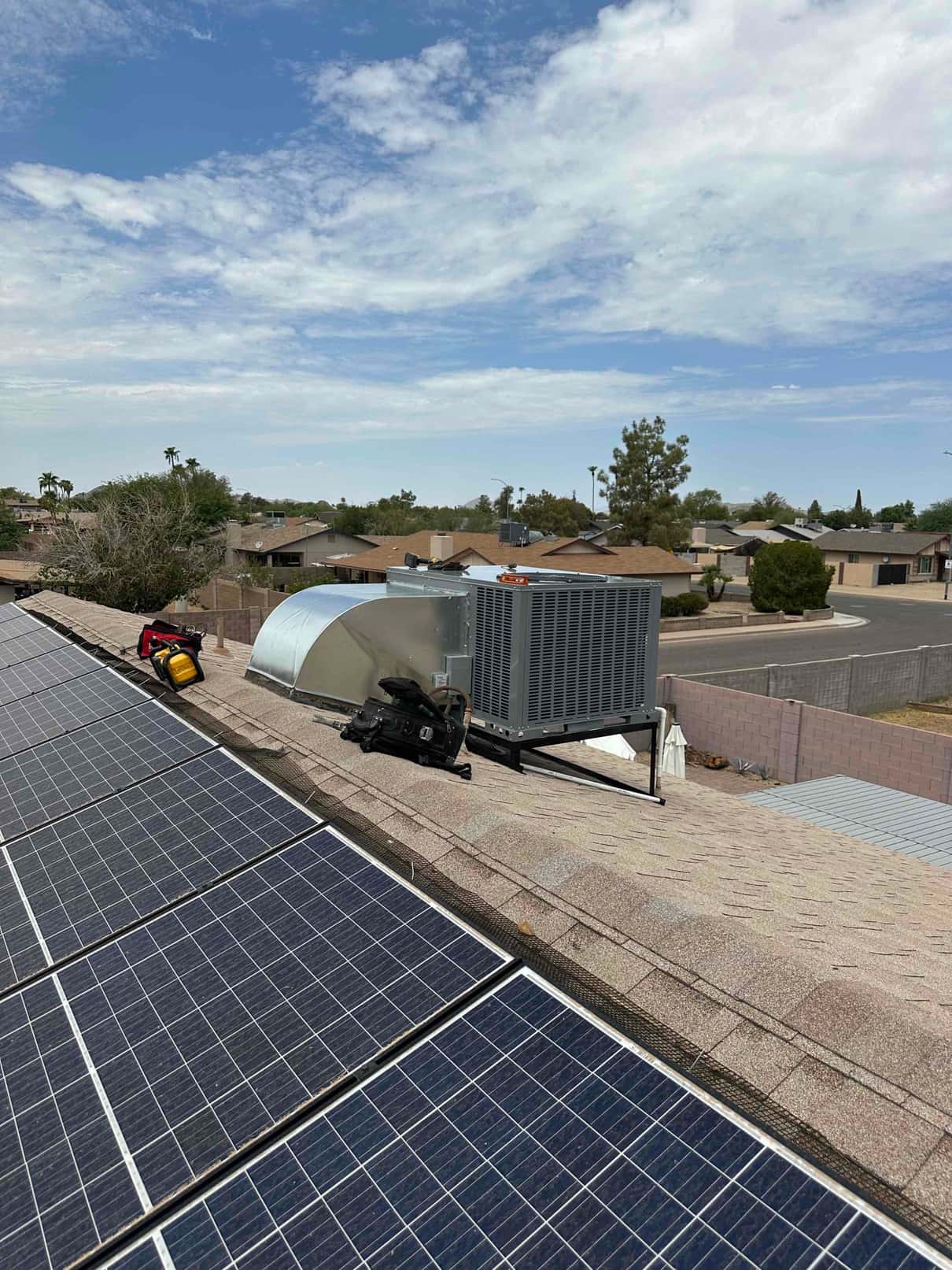 New rooftop package unit set on a steel stand with connected curb and nearby tools, shown alongside existing solar panels.