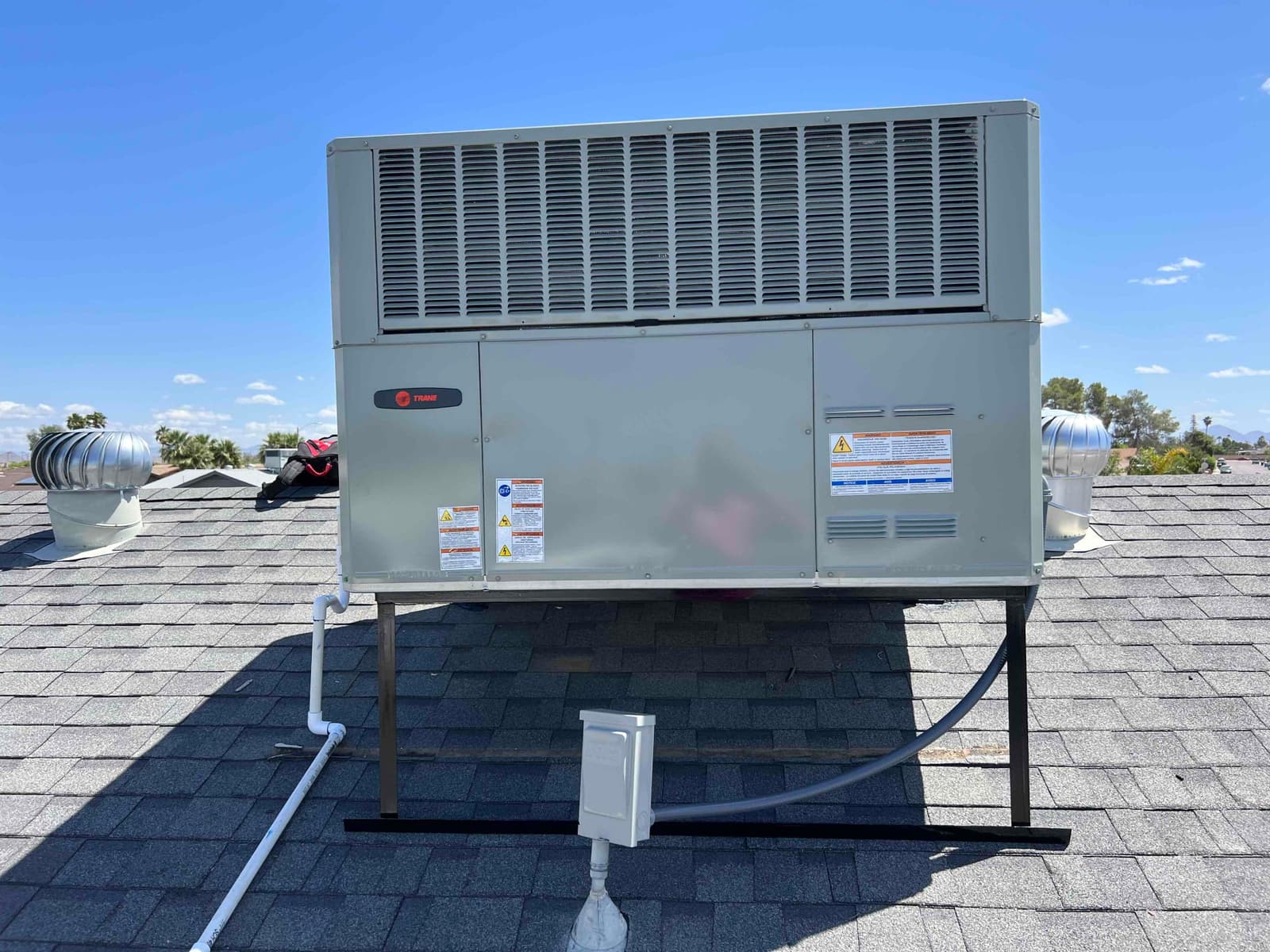 New rooftop packaged HVAC unit installed on stands with sealed drain line, electrical whip, and roof jack visible.