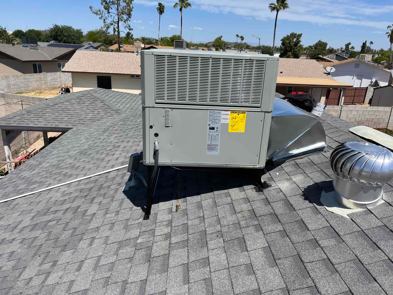 New rooftop packaged HVAC unit set on support stands with curb connection, sealed roof penetration, and nearby turbine vent visible.