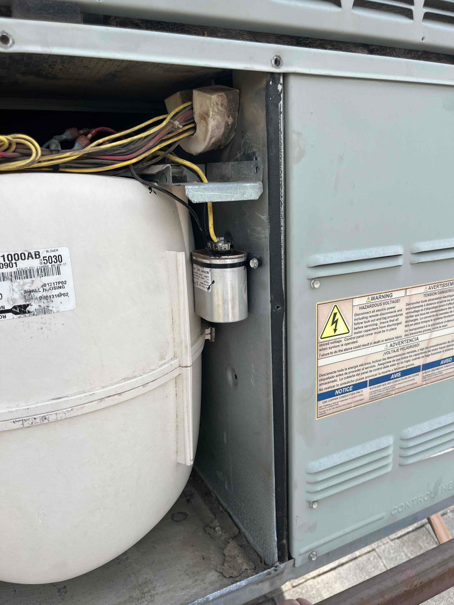 New run capacitor mounted inside the condenser panel with connected yellow and black wires beside the compressor housing.