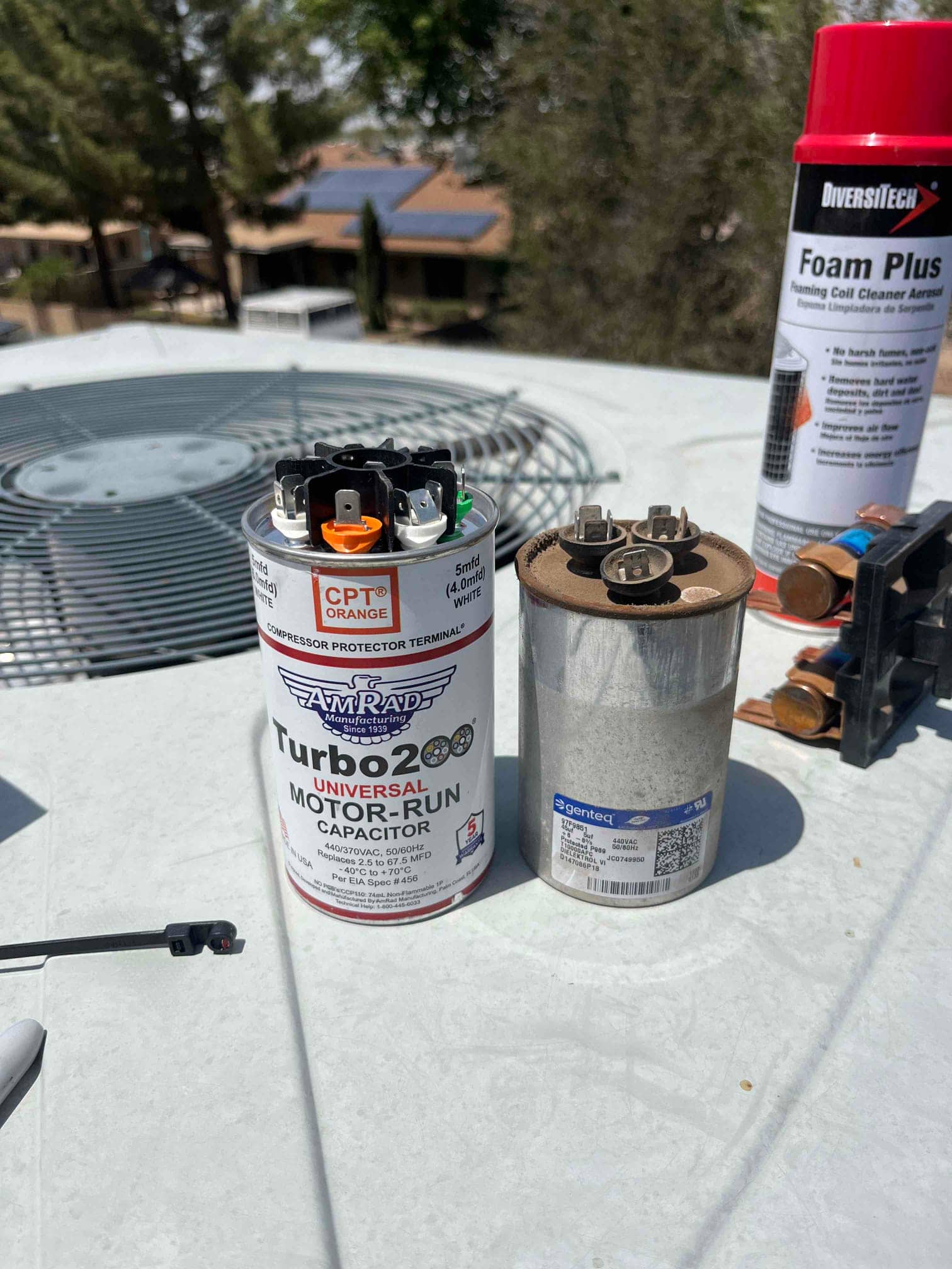 Old dual-run capacitor removed beside new Turbo 200 universal motor-run capacitor on the condenser unit top, with contactor and coil cleaner nearby.
