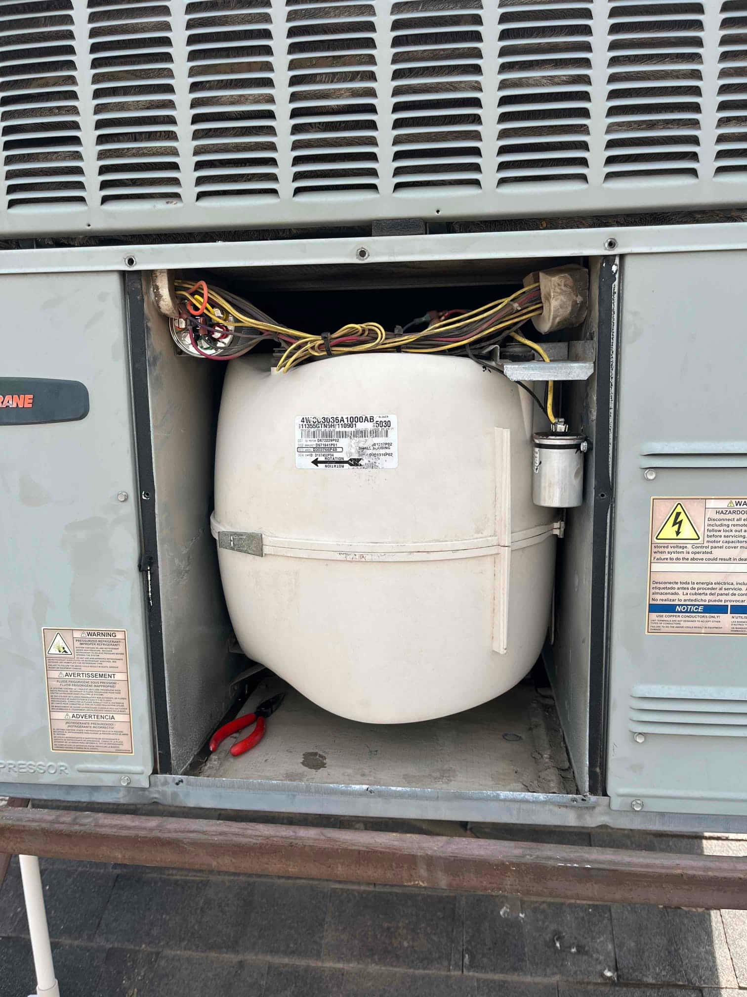 Outdoor condenser access panel open, showing wiring, a run capacitor mounted at right, and a large white accumulator or tank.