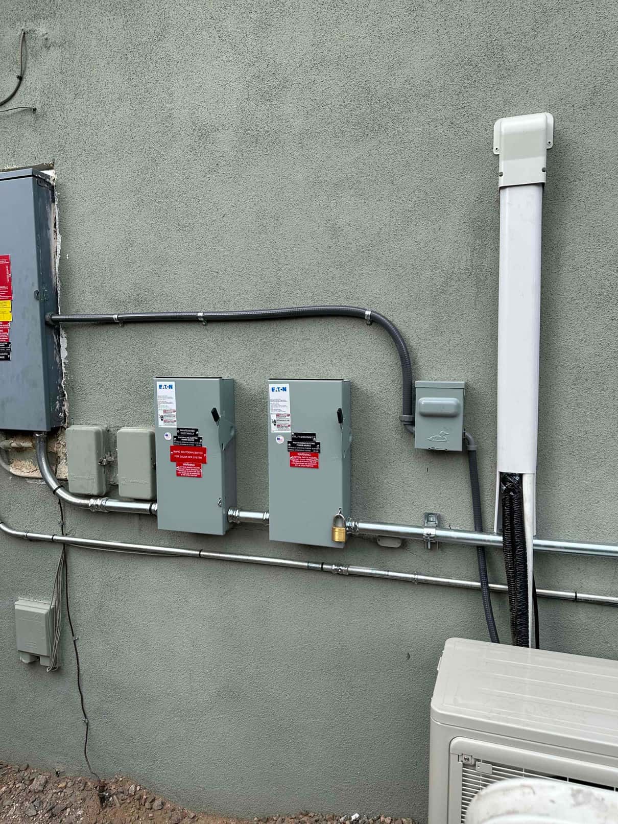 Outdoor installation shows mounted disconnects, sealed conduit, line-hide covering the refrigerant lines, and the mini-split condenser below.