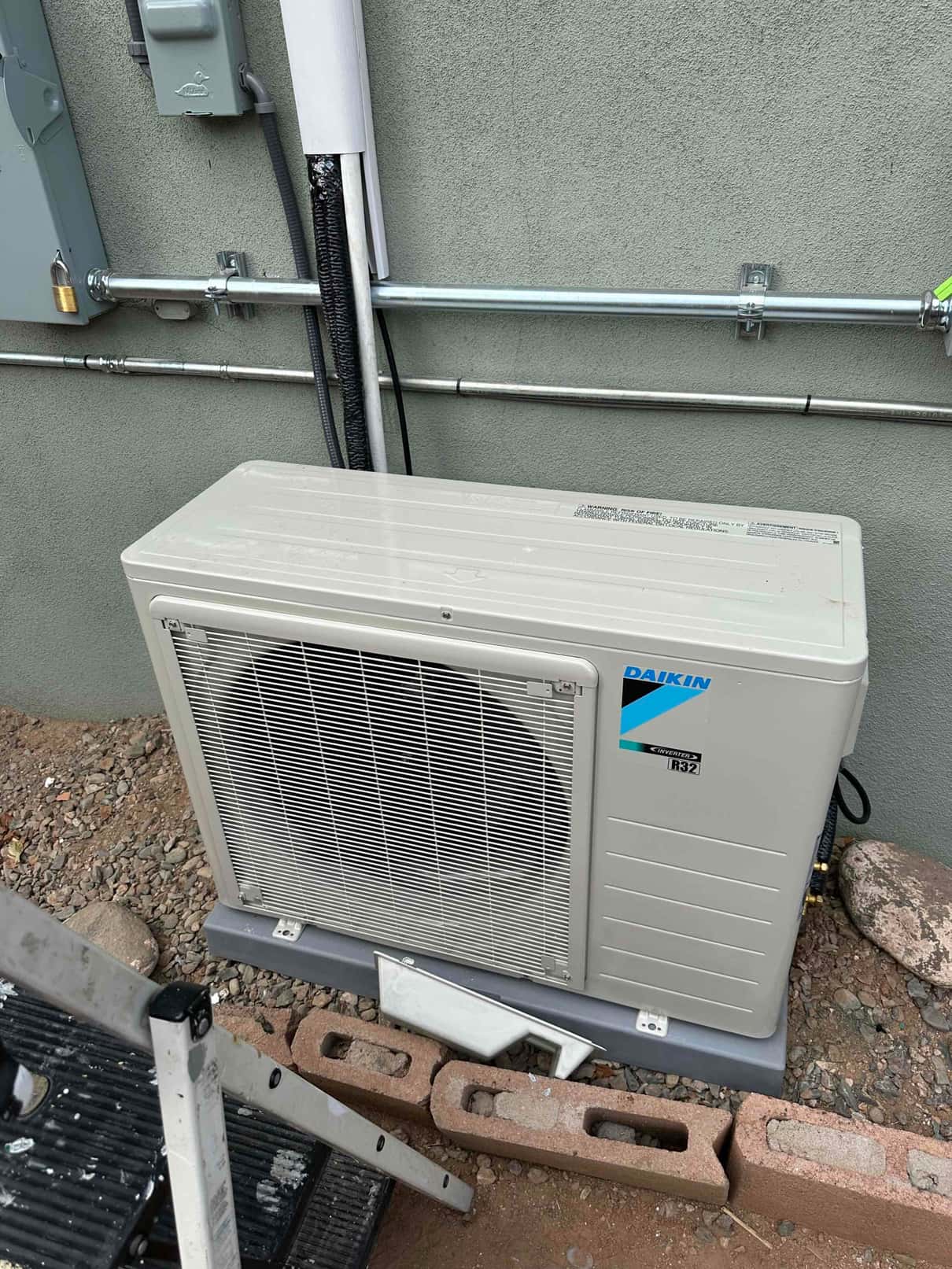 Outdoor mini‑split condenser set on a level pad with conduit, line‑set cover, and electrical disconnect installed on the wall.