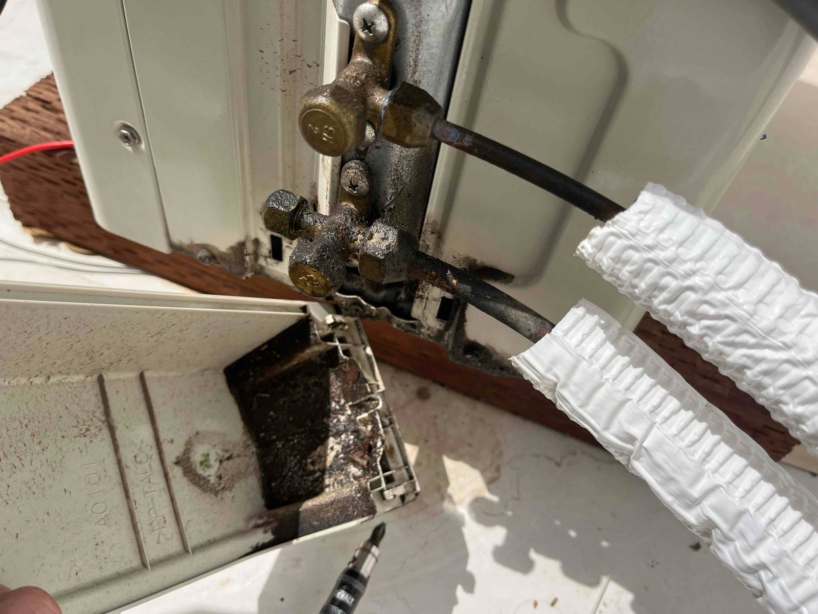 Outdoor refrigerant service valves and line set connections show rust and corrosion near an open electrical disconnect with debris inside.