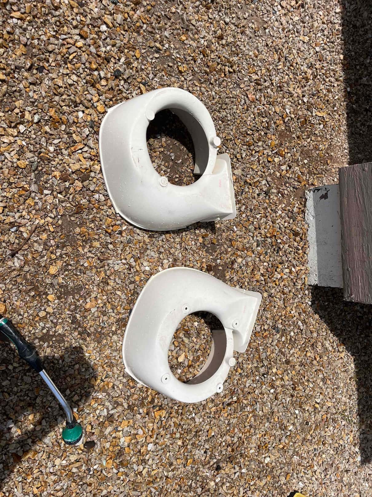 Two plastic condenser fan shrouds removed and set on gravel during air conditioner cleaning.