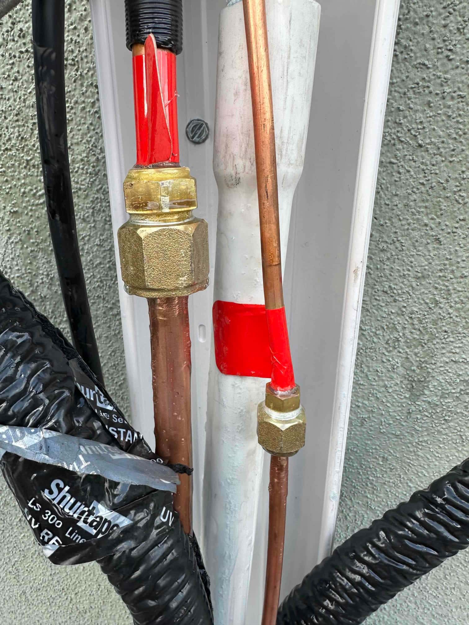 Refrigerant line set connections inside a line-hide channel, with insulated suction line and brazed and flared fittings neatly secured.