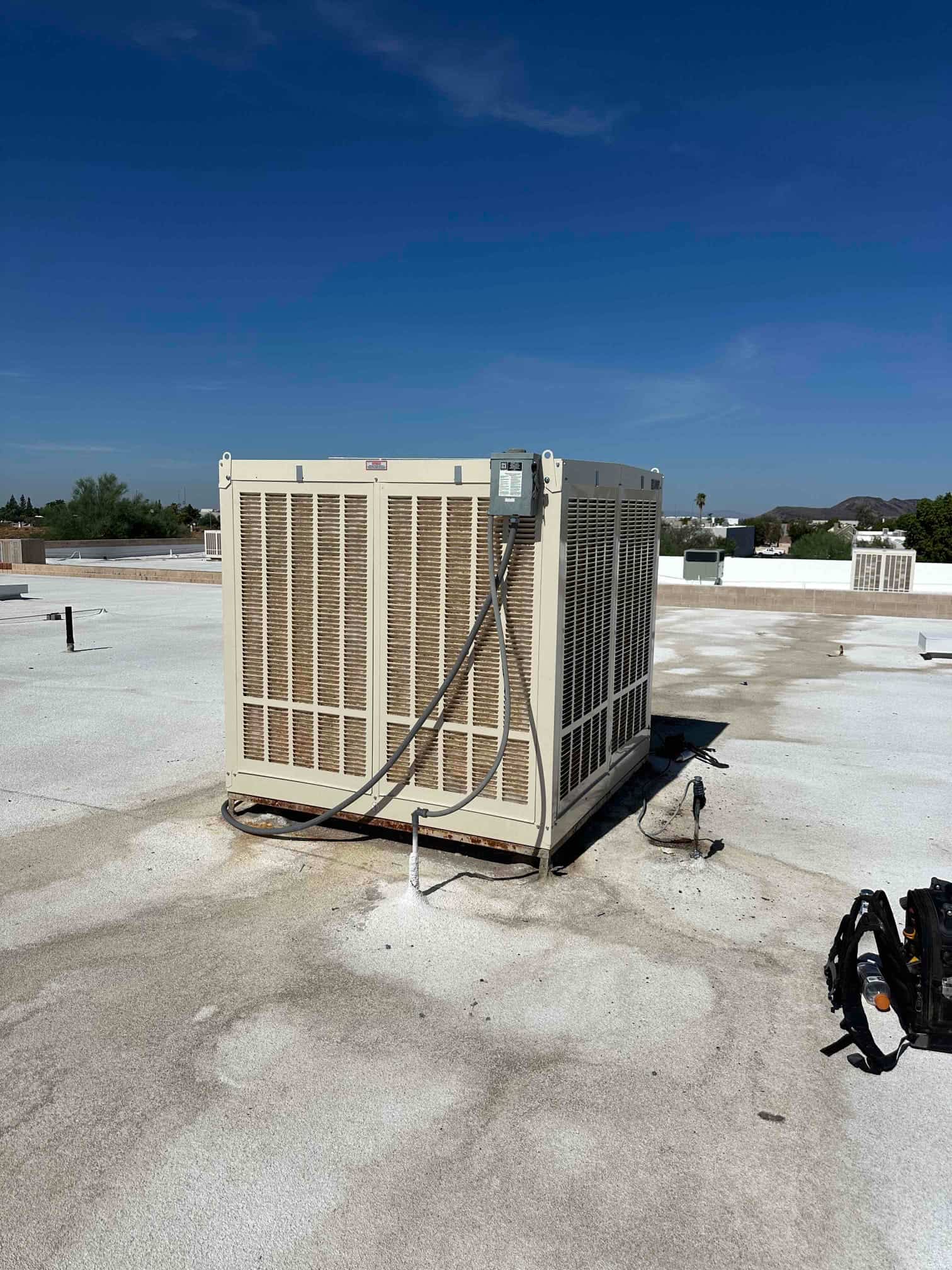 Rooftop evaporative cooler installation shown in place with electrical disconnect and drain line visible on the roof surface.
