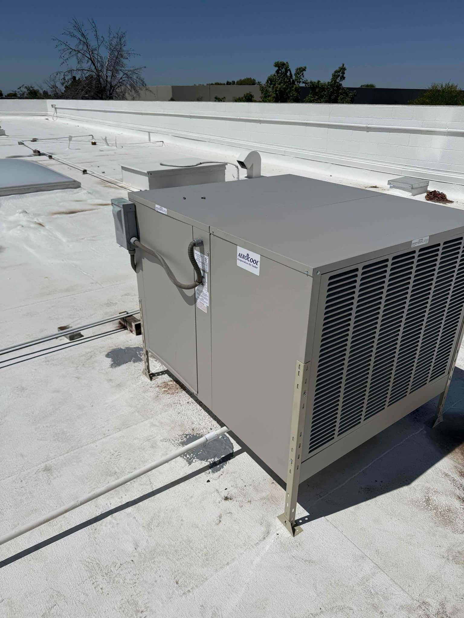 Rooftop evaporative cooler installation shown on standoff legs with electrical disconnect and drain line routed across the roof.