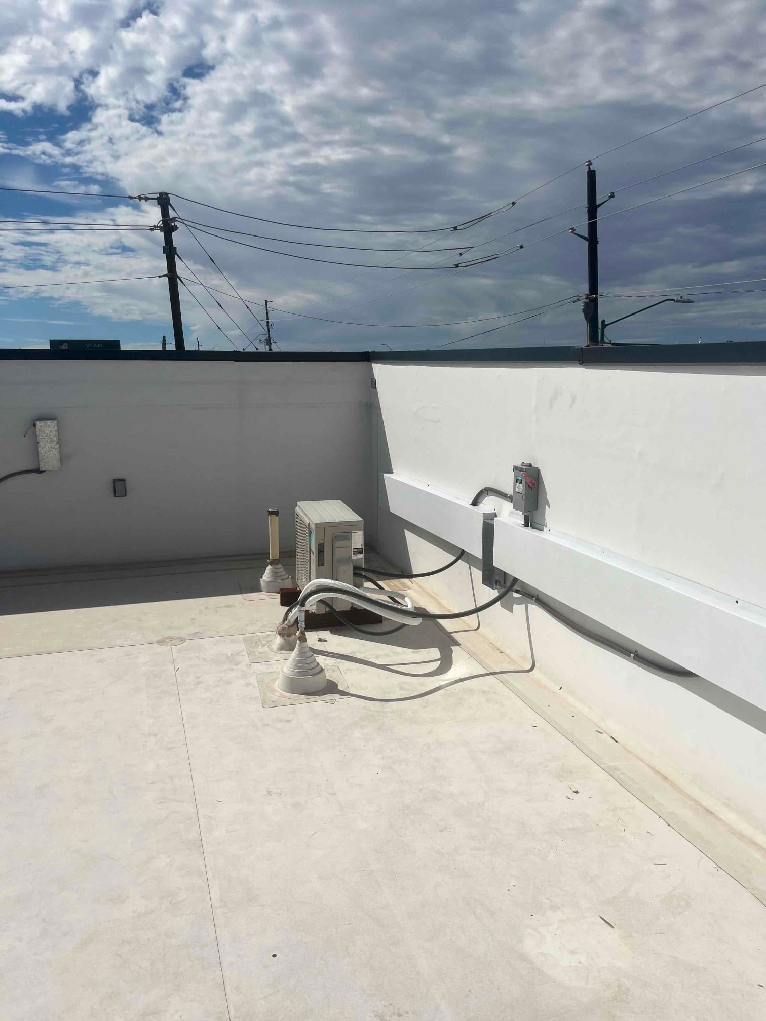 Rooftop mini-split condenser with insulated line set, electrical disconnect, and condensate drain piping installed along the parapet wall.