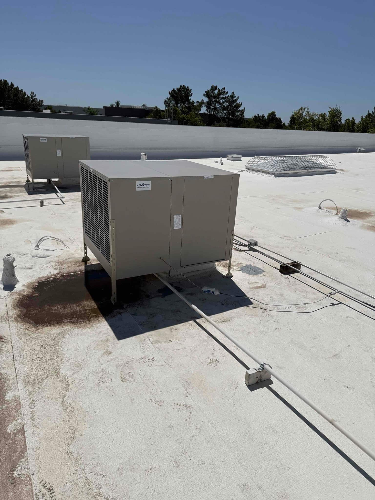 Rooftop packaged HVAC unit newly set on curbs with condensate drain piping routed across the roof surface.