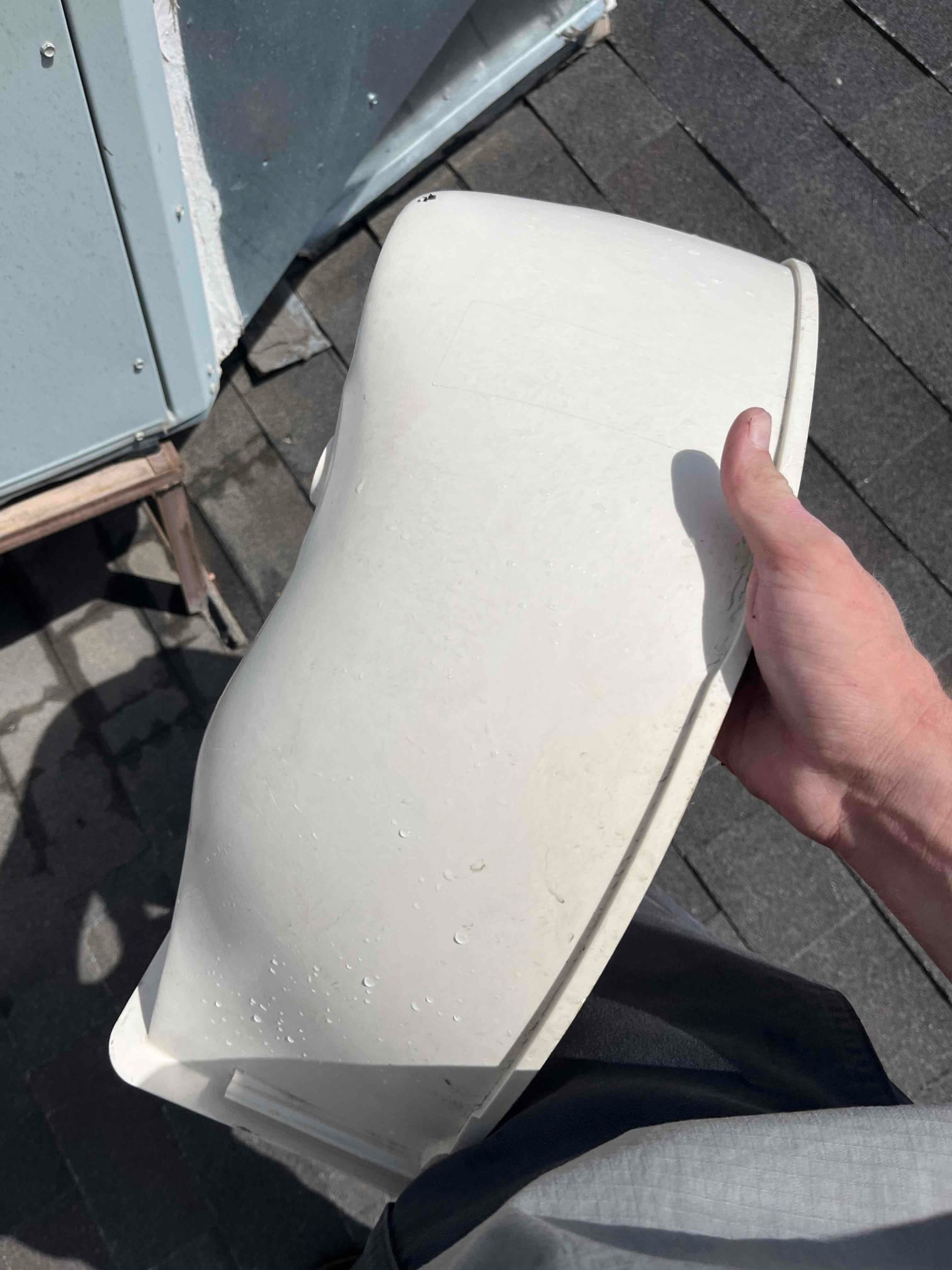 Technician holds a warped plastic fan shroud or blower housing removed from rooftop HVAC equipment, showing deformation and water droplets.