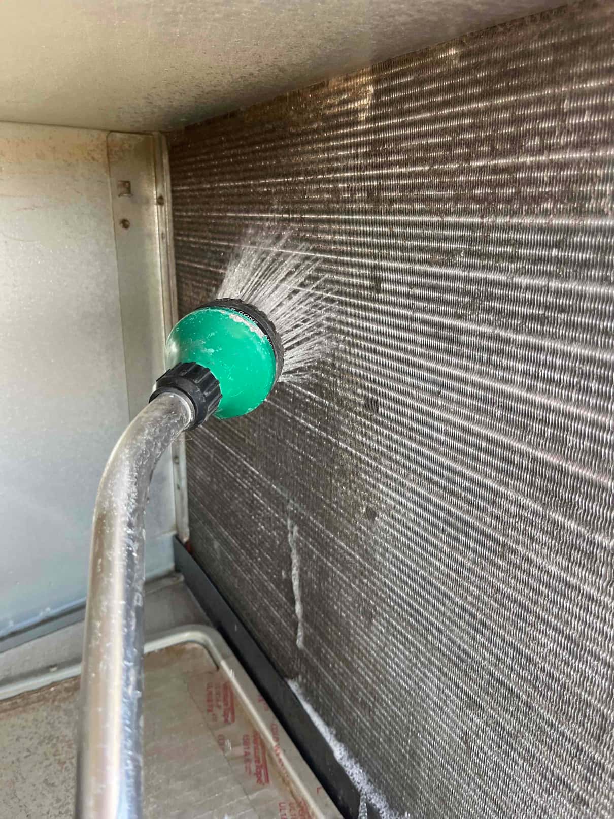 Technician rinses an evaporator coil with a spray nozzle, flushing debris from the fin surface during a super clean.