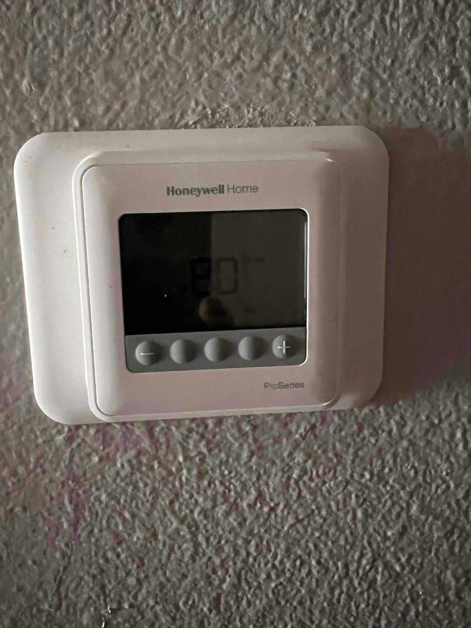 Wall-mounted digital thermostat installed and powered on, showing the home control interface with adjustment buttons.