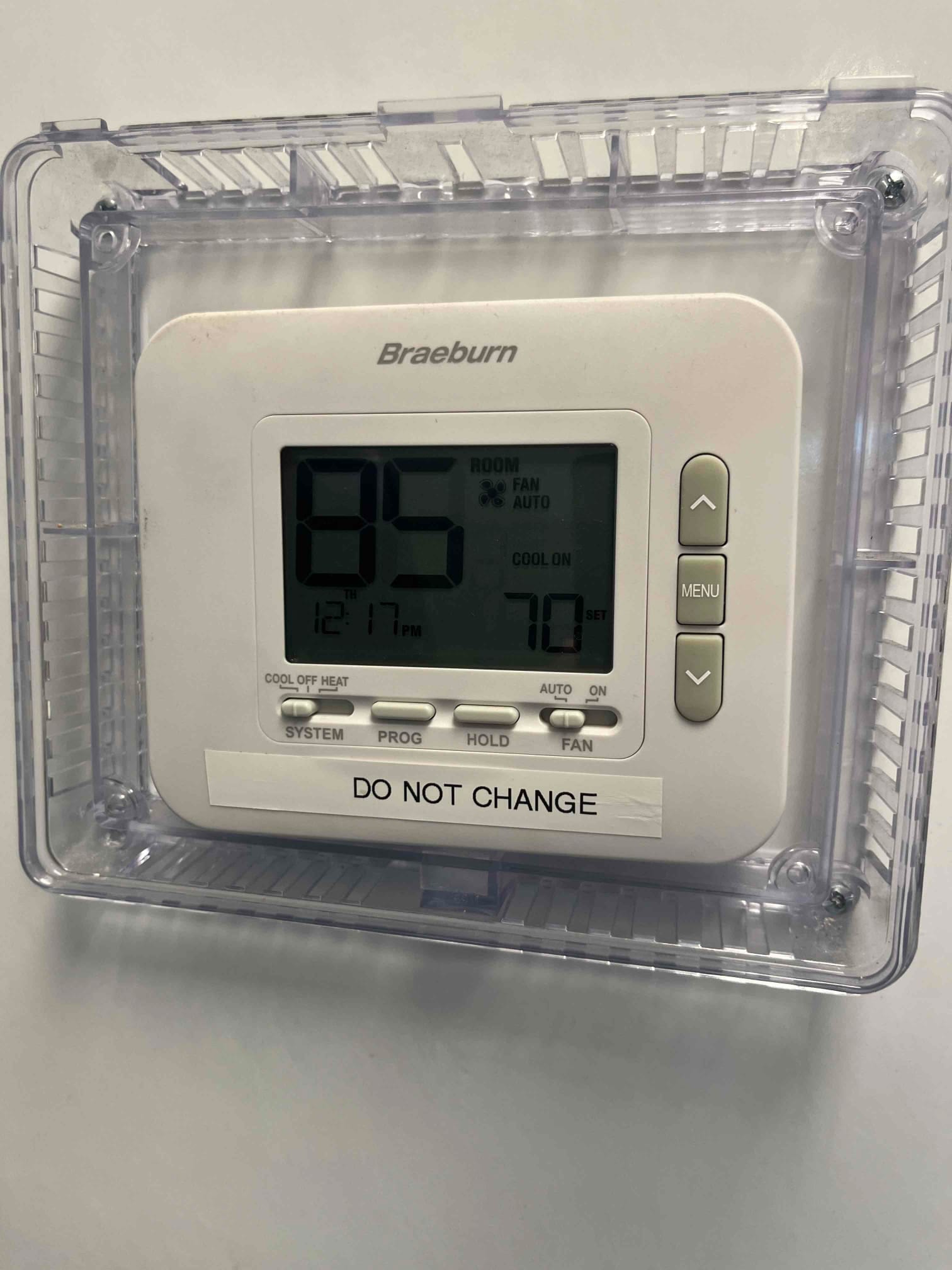 Wall-mounted digital thermostat in a protective lockbox, display showing room temperature, setpoint, operating mode, and fan status.