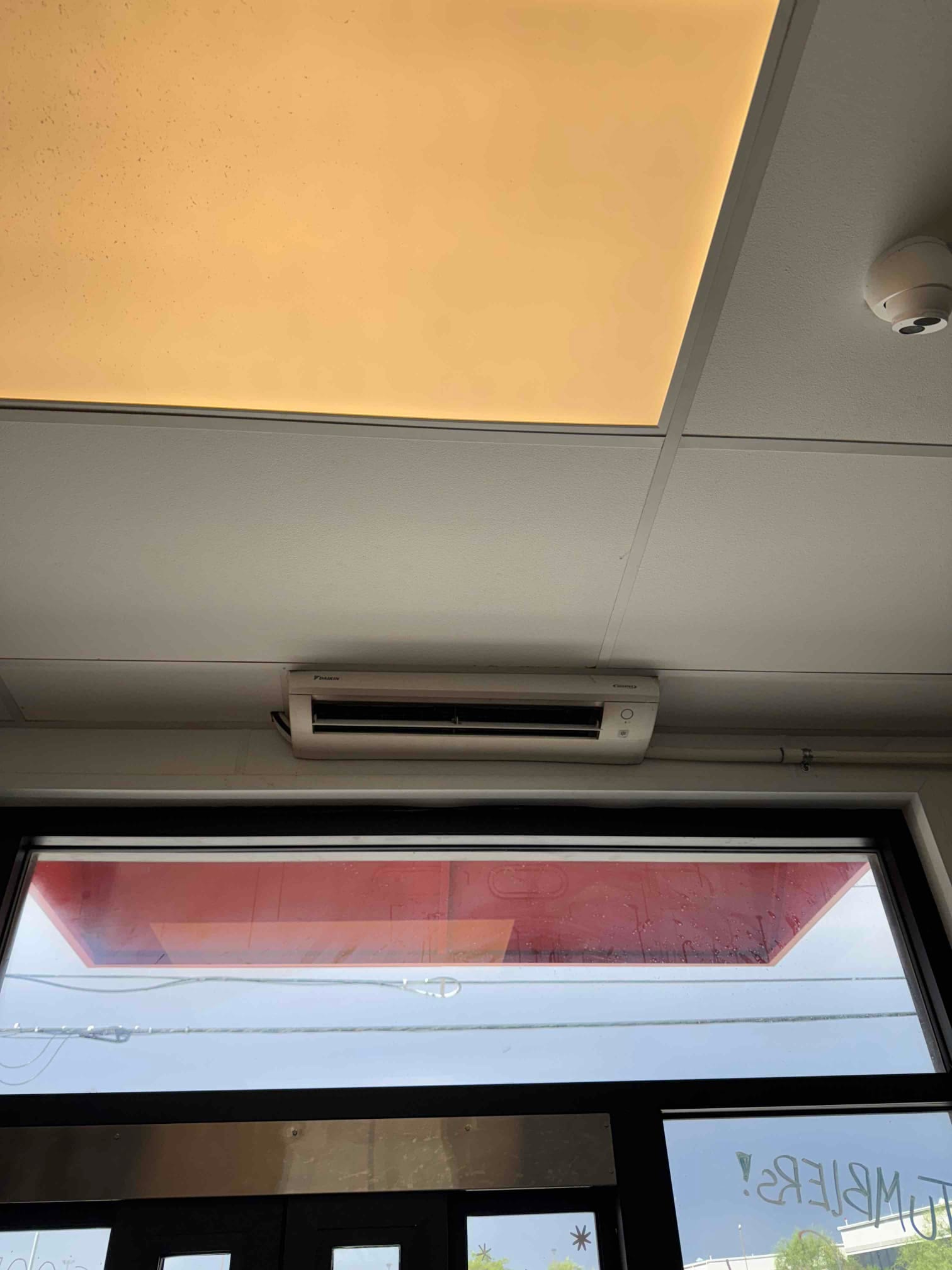 Wall-mounted ductless indoor unit above a glass entry door, showing clean grille and surrounding ceiling panels.