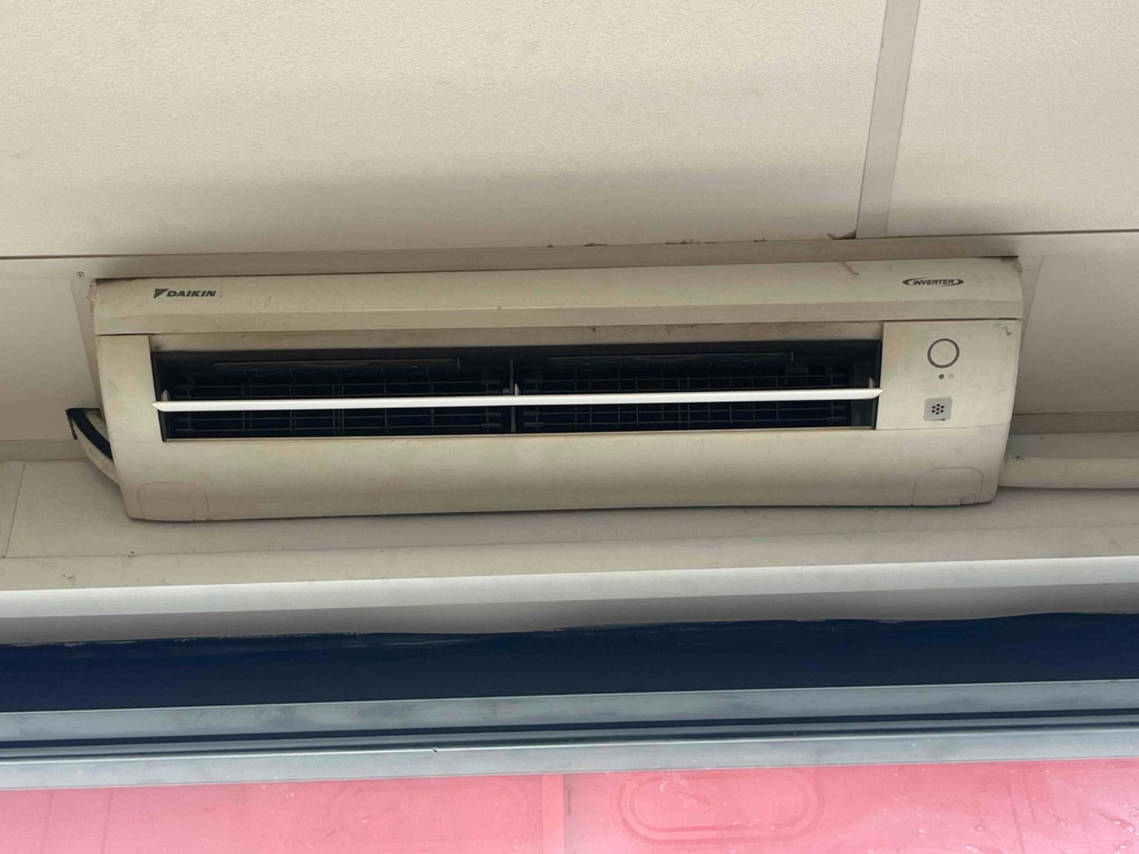 Wall-mounted indoor air conditioning unit with front panel closed and supply louvers visible, installed beneath a ceiling.