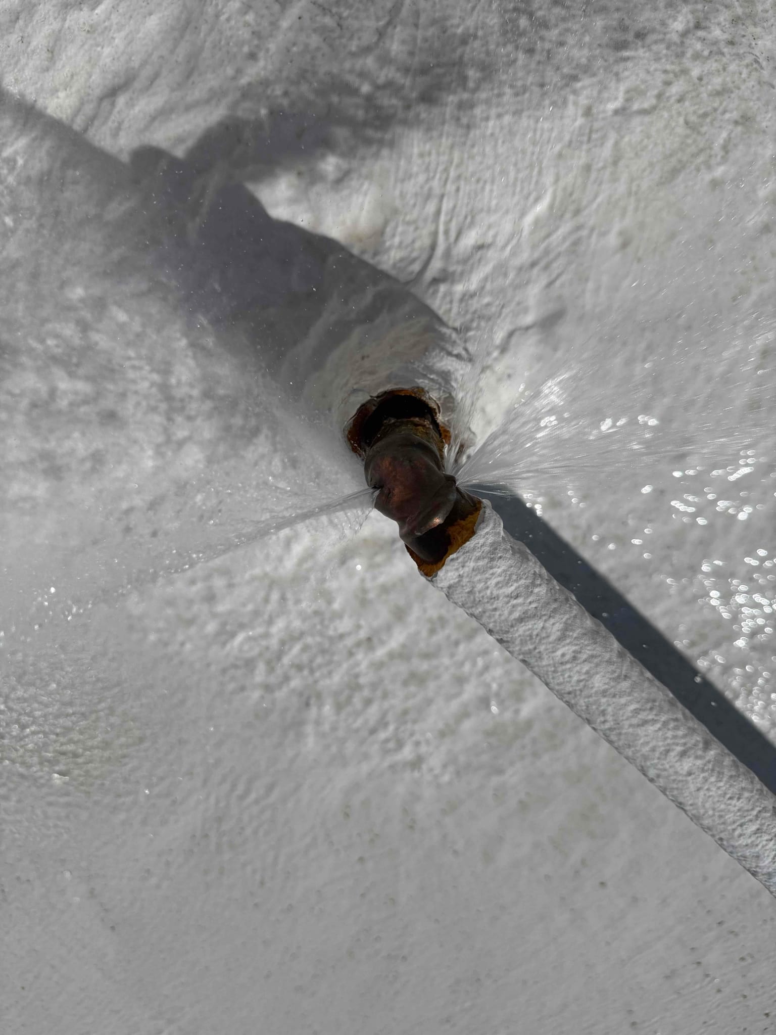 Water sprays from a small nozzle or fitting on a white evaporative cooler surface during operation.