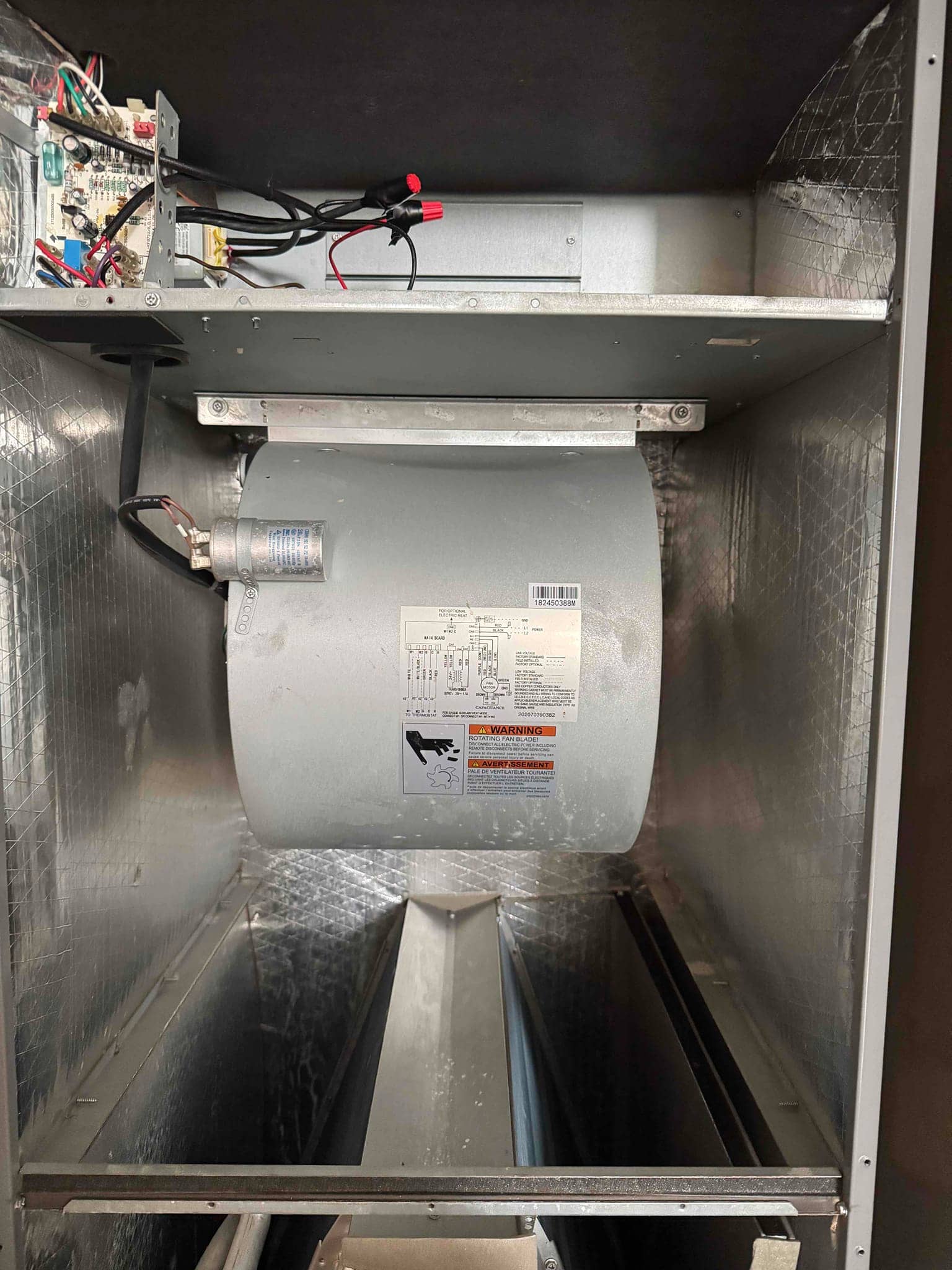 Air handler interior showing blower assembly, run capacitor mounted on housing, control board wiring, and clean insulated cabinet surfaces.