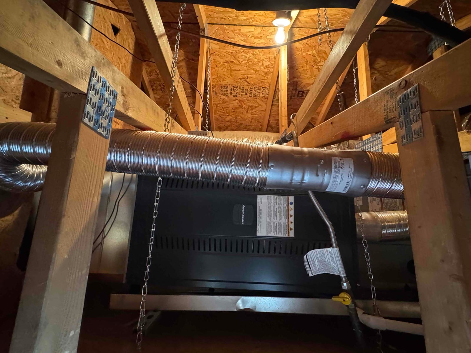 Air handler suspended in attic with insulated flex ducts, gas shutoff valve, and condensate drain connections visible.