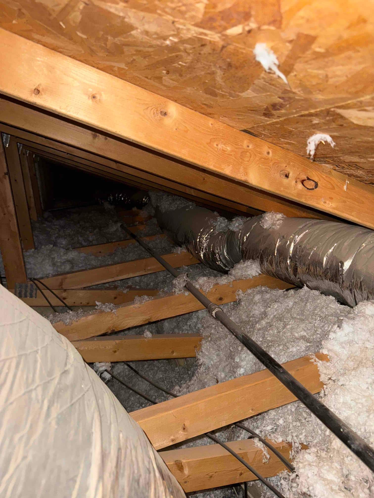 Attic crawlspace shows flexible insulated ductwork routed over joists with blown-in insulation covering the attic floor.