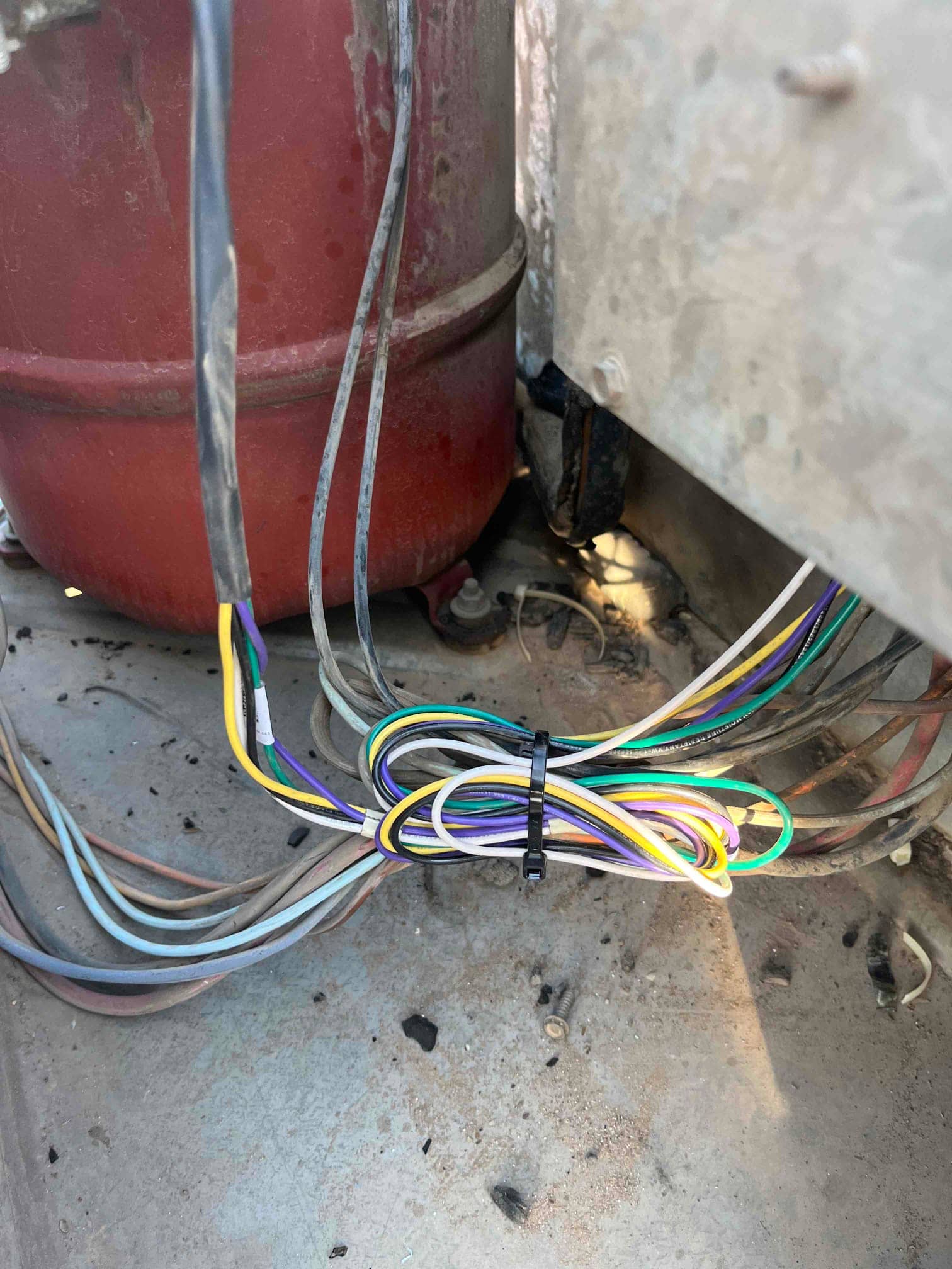 Bundled condenser wiring secured with a zip tie inside the outdoor unit near the compressor housing and cabinet base.