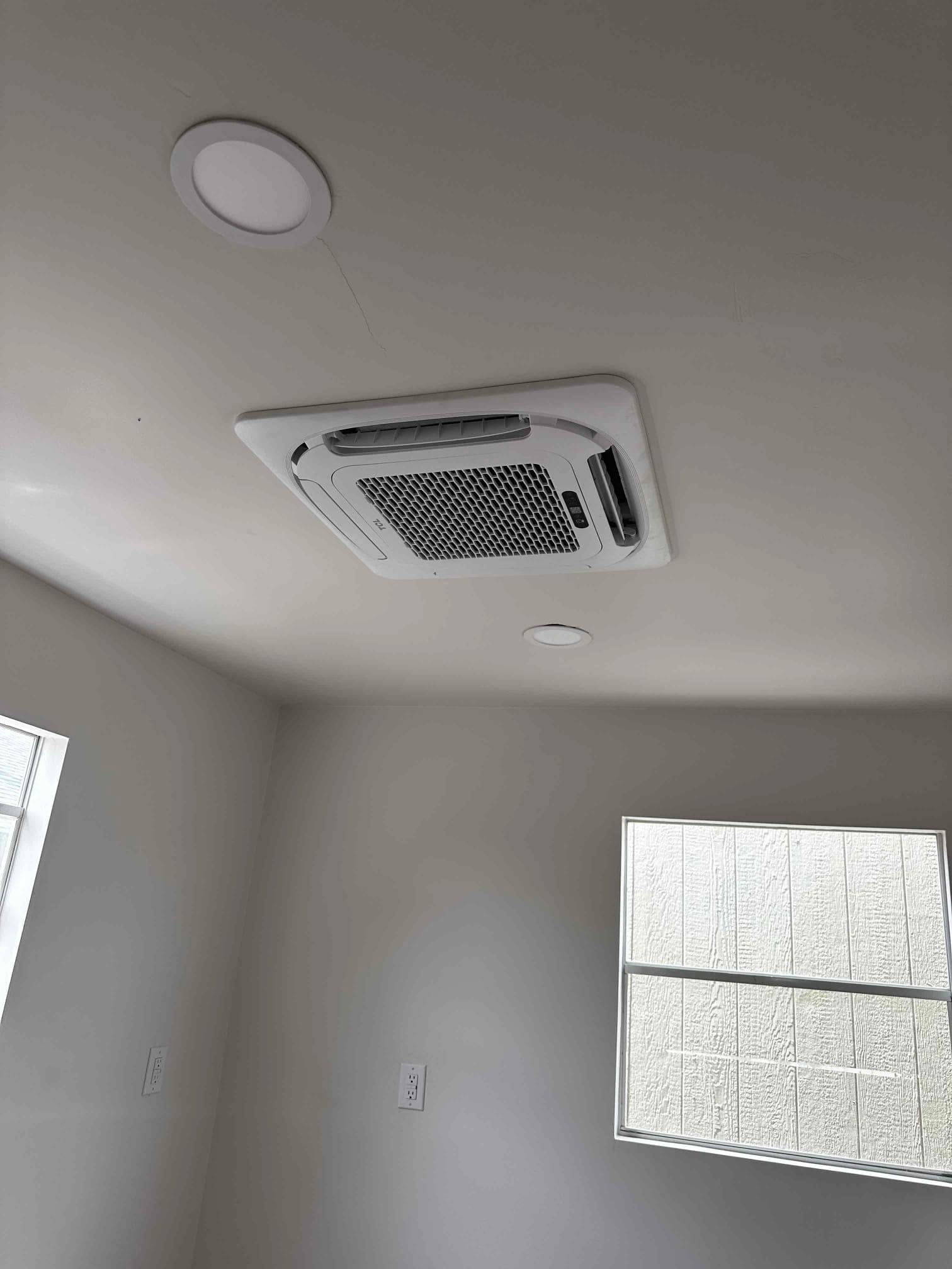 Ceiling cassette indoor unit neatly installed flush with the ceiling alongside recessed lights in a finished room.