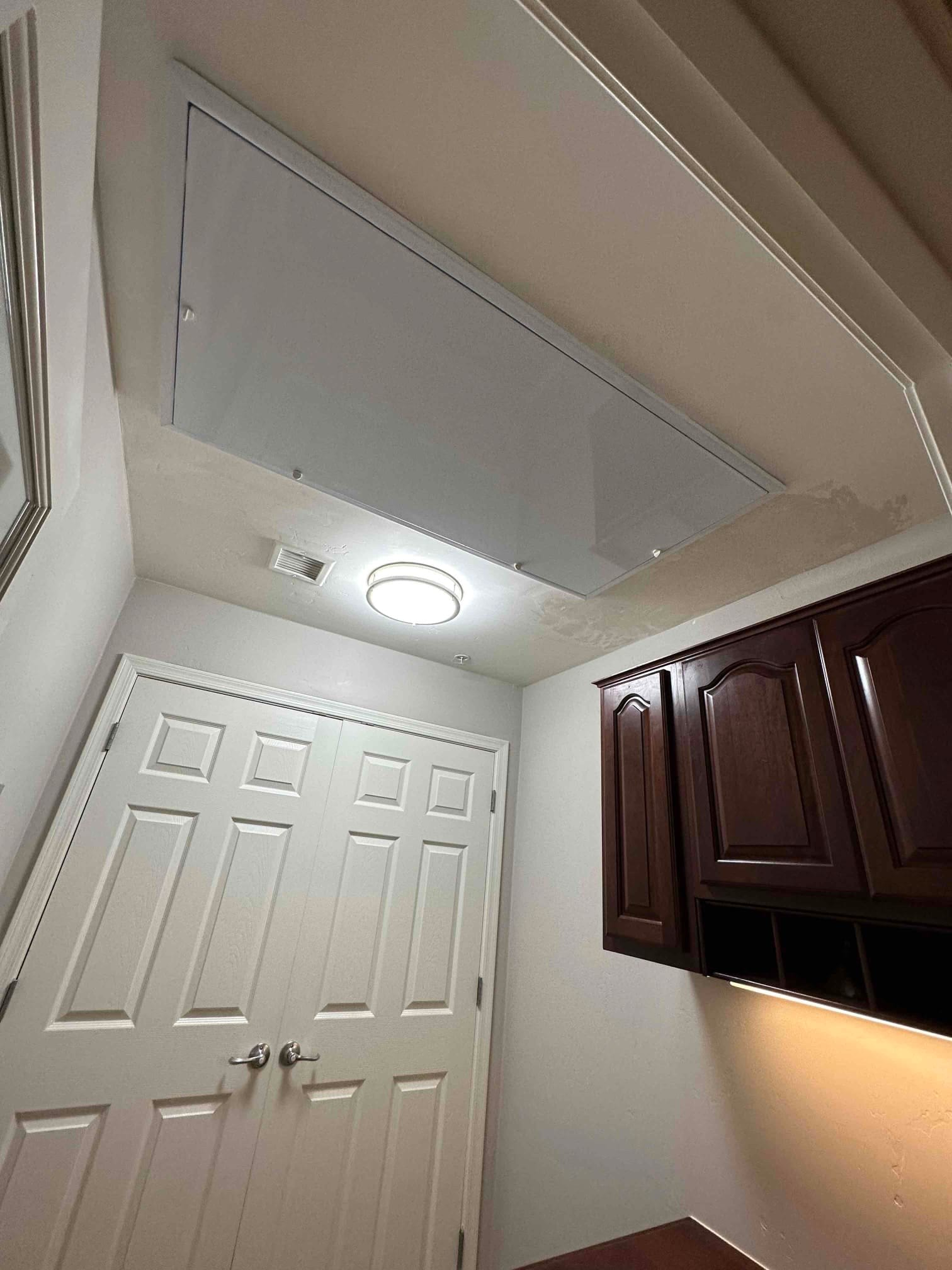 Ceiling-mounted air handler with finished return grille panel installed flush in a hallway ceiling near cabinets and a closet.