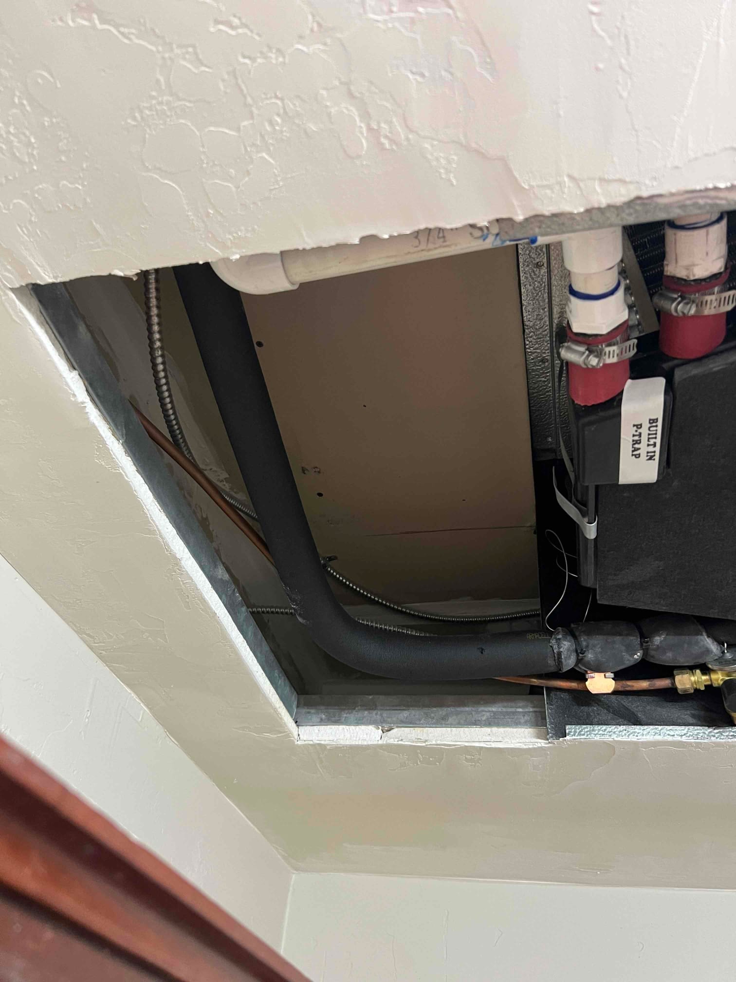 Ceiling-mounted air handler with insulated refrigerant lines, condensate drain with built-in trap, and copper line set connections visible.