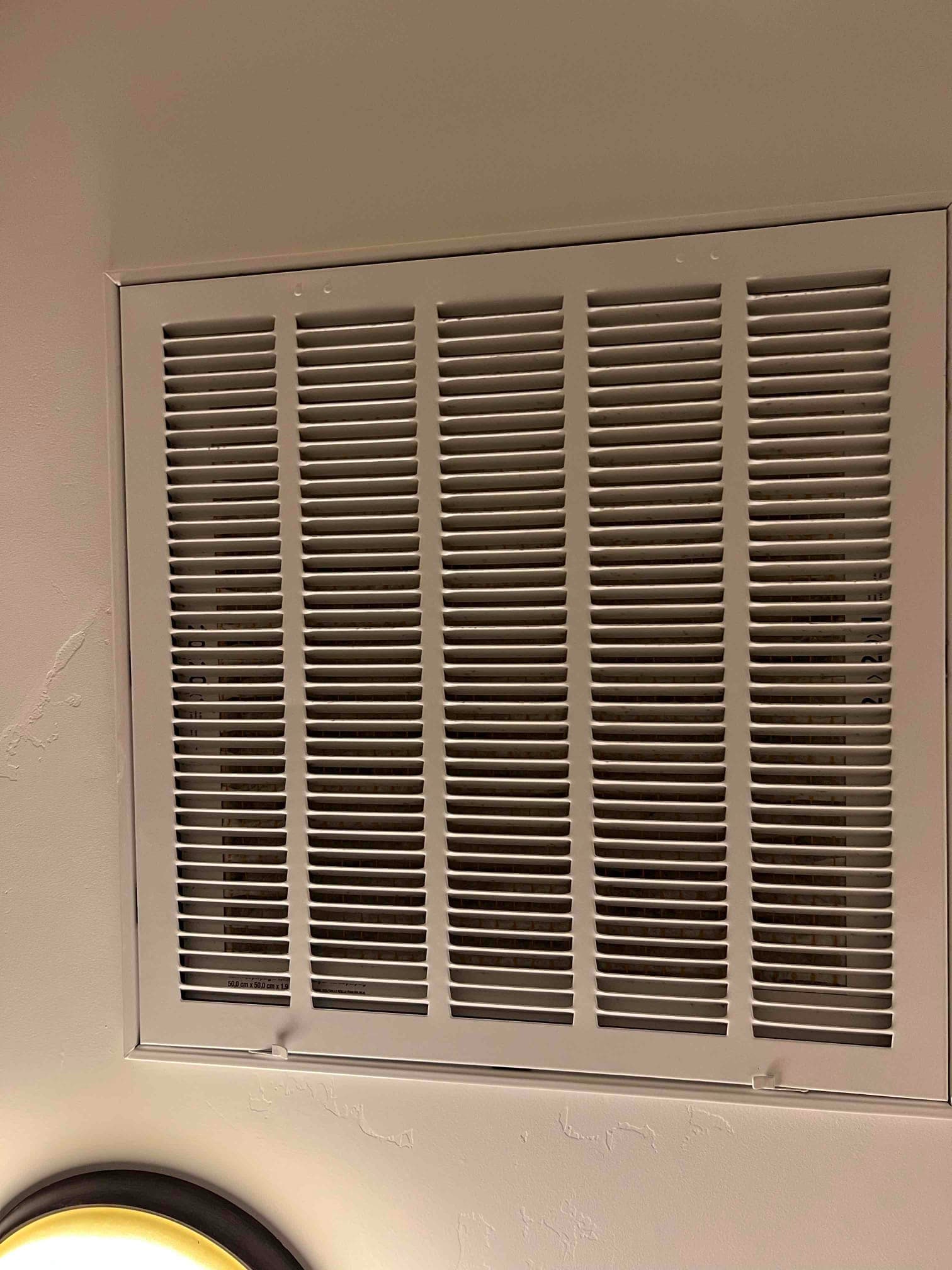 Ceiling-mounted return air grille installed flush with surrounding surface, showing clean louvers and secured fasteners at the frame.