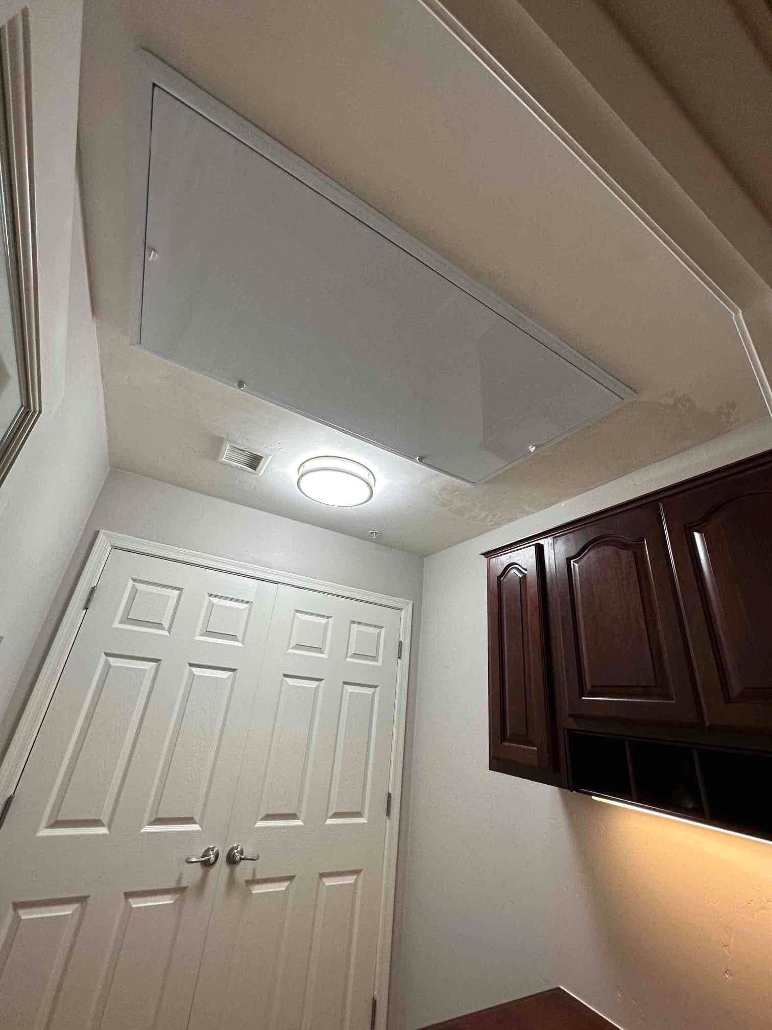 Ceiling-mounted return grille and access panel finished in a laundry area, with nearby cabinets and doors showing the completed installation.
