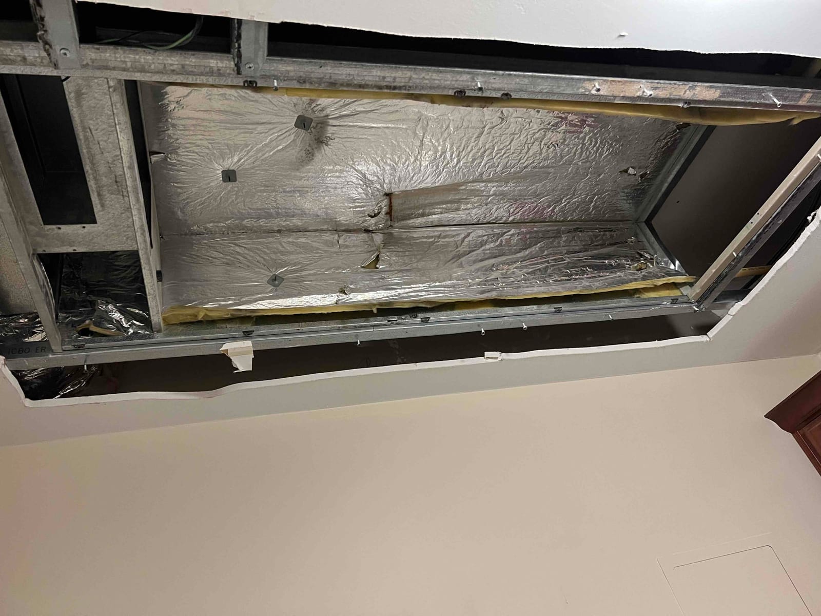 Ceiling opening shows insulated ductwork and metal framing around a recessed air handler location during installation.