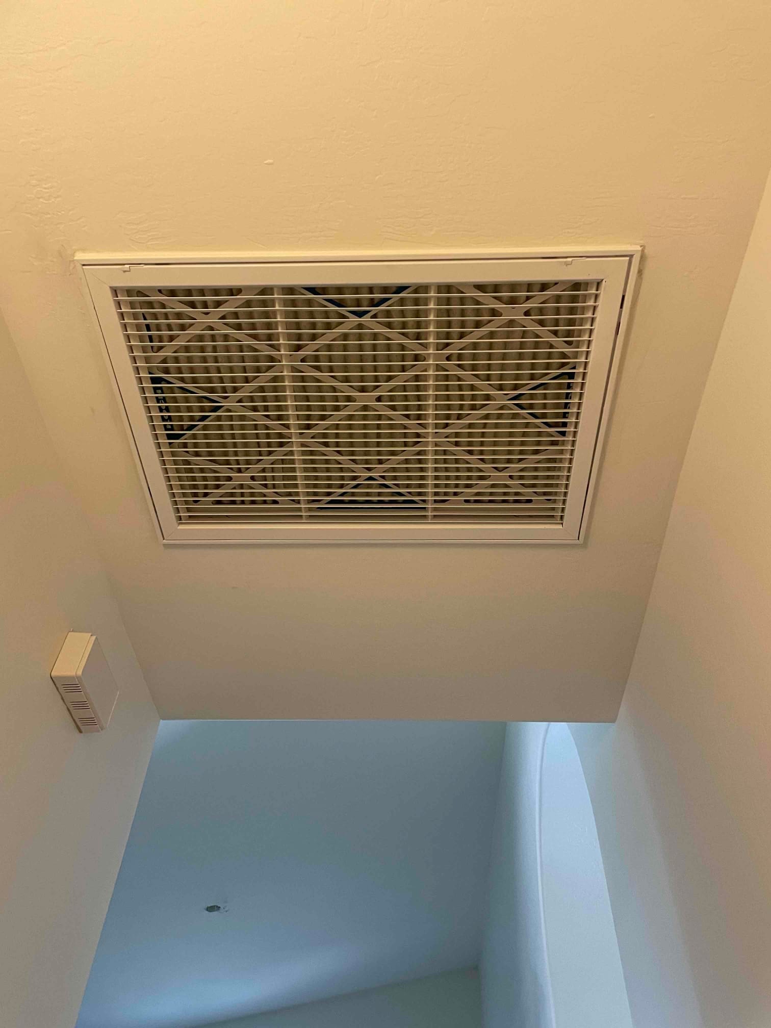 Ceiling return grille with new air filter installed in a hallway ceiling, showing clean trim and secure fasteners.