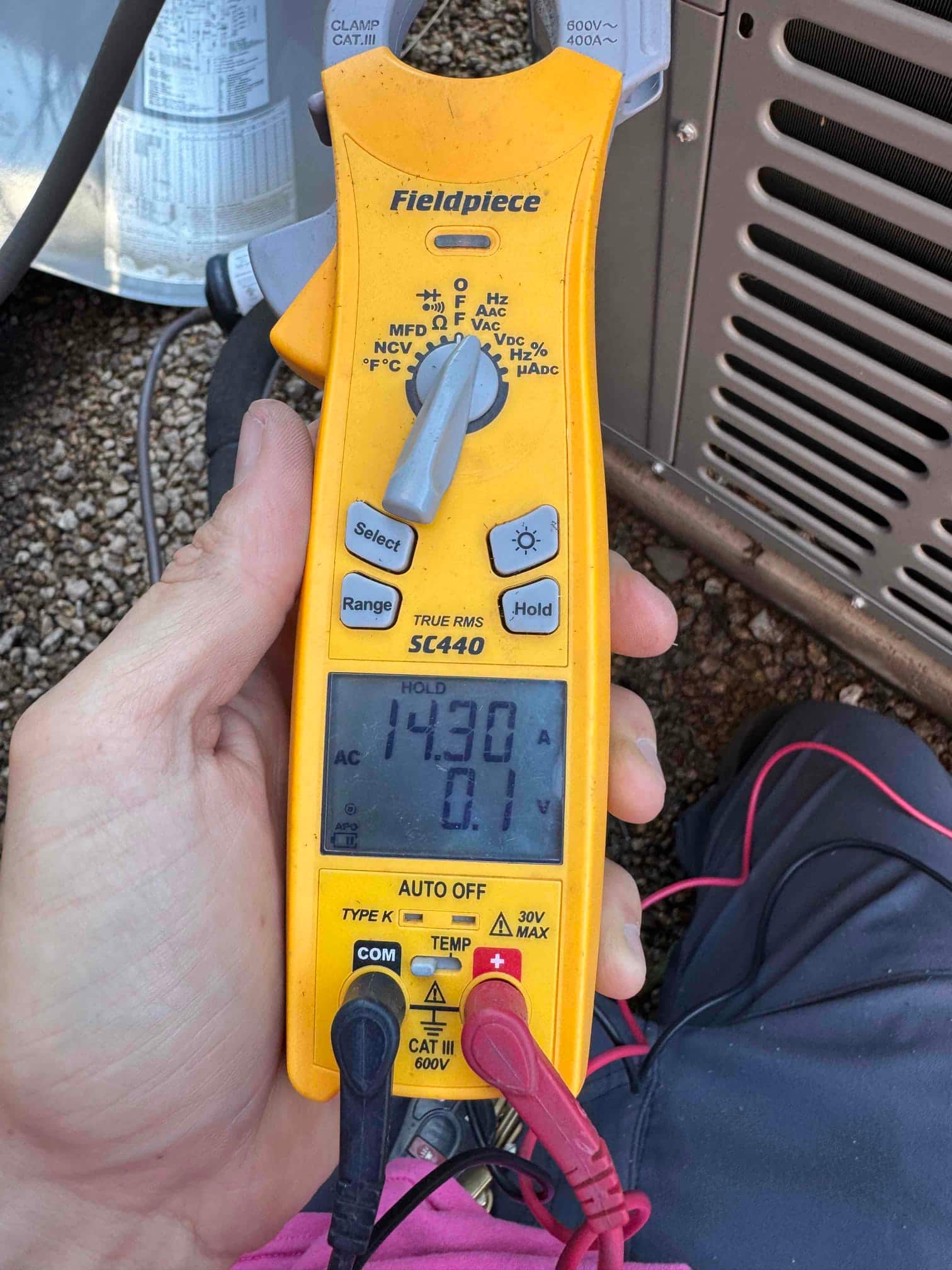 Clamp meter measures 14.30 A on the clamped conductor at the outdoor unit during air conditioning repair.