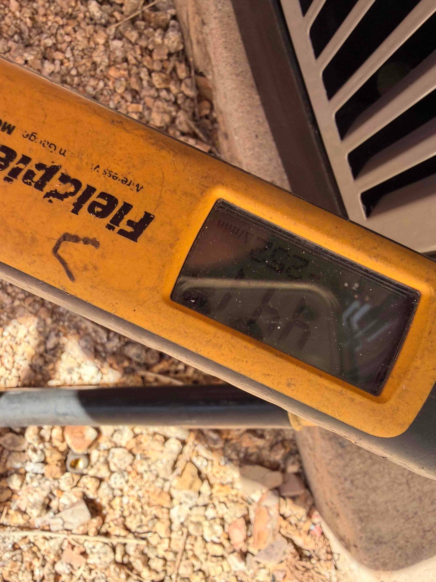 Clamp meter rests near the outdoor unit with the display partially visible during electrical checks at the condenser.